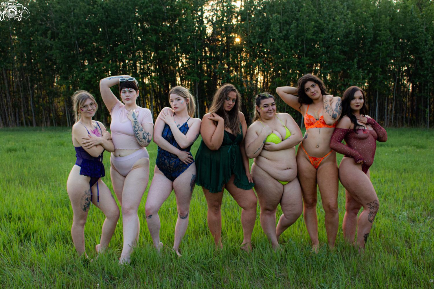 Group of people in colorful swimsuits posing together on a grassy field with trees in background at sunset.