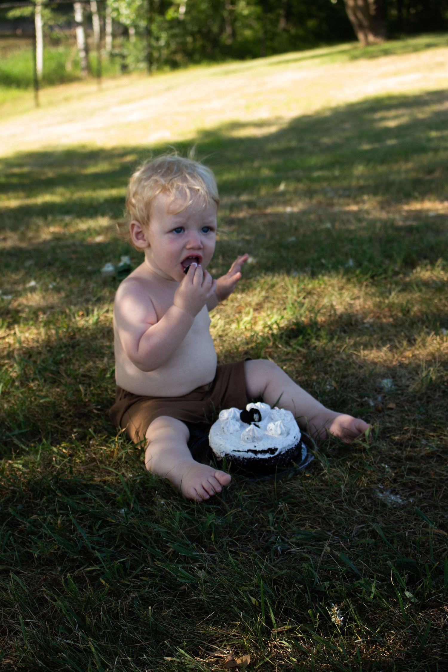 Baby enjoys messy cake smash photo session outdoors on grass.