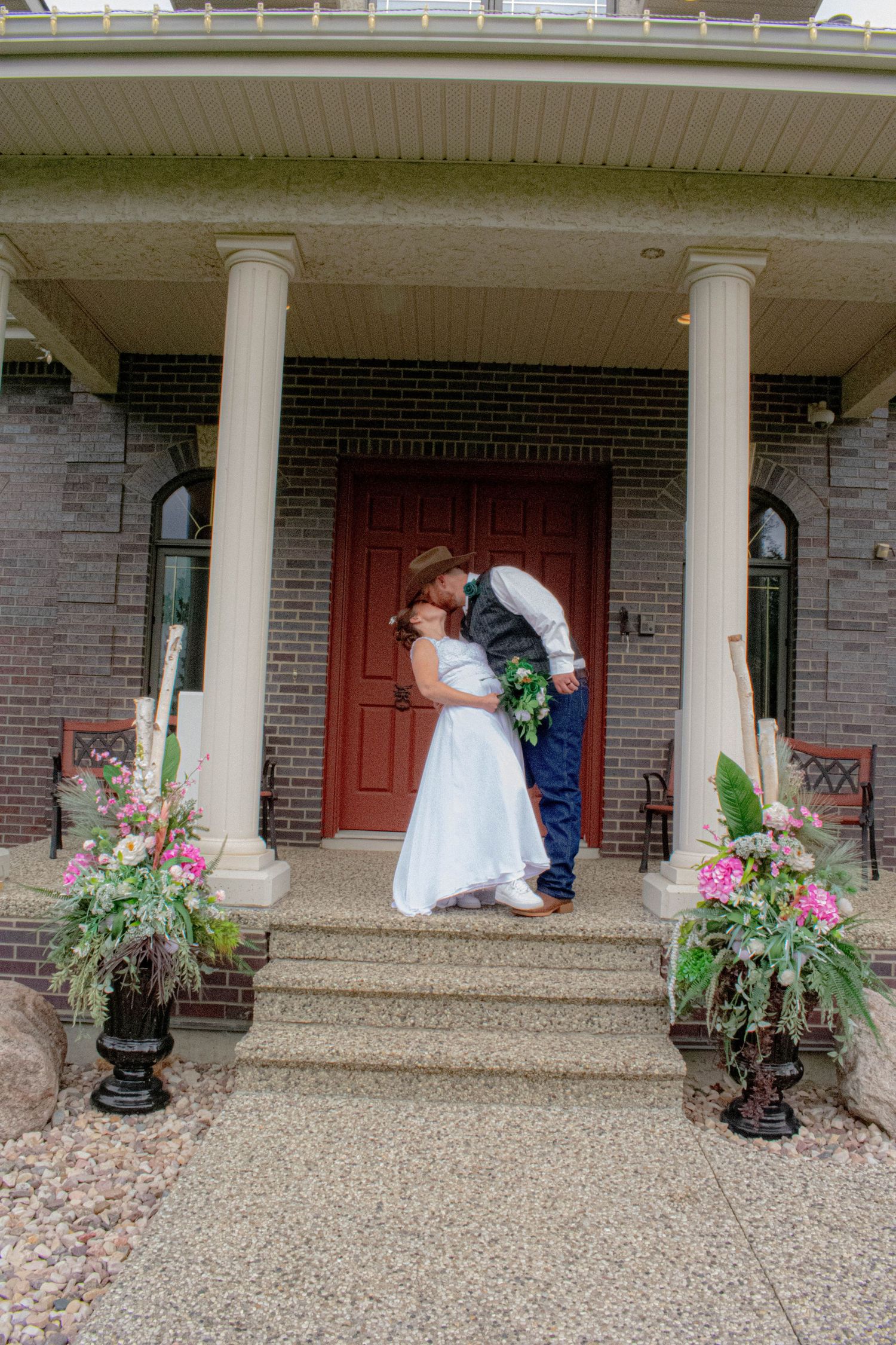 Wedding couple sharing intimate moment on brick porch with floral decorations.