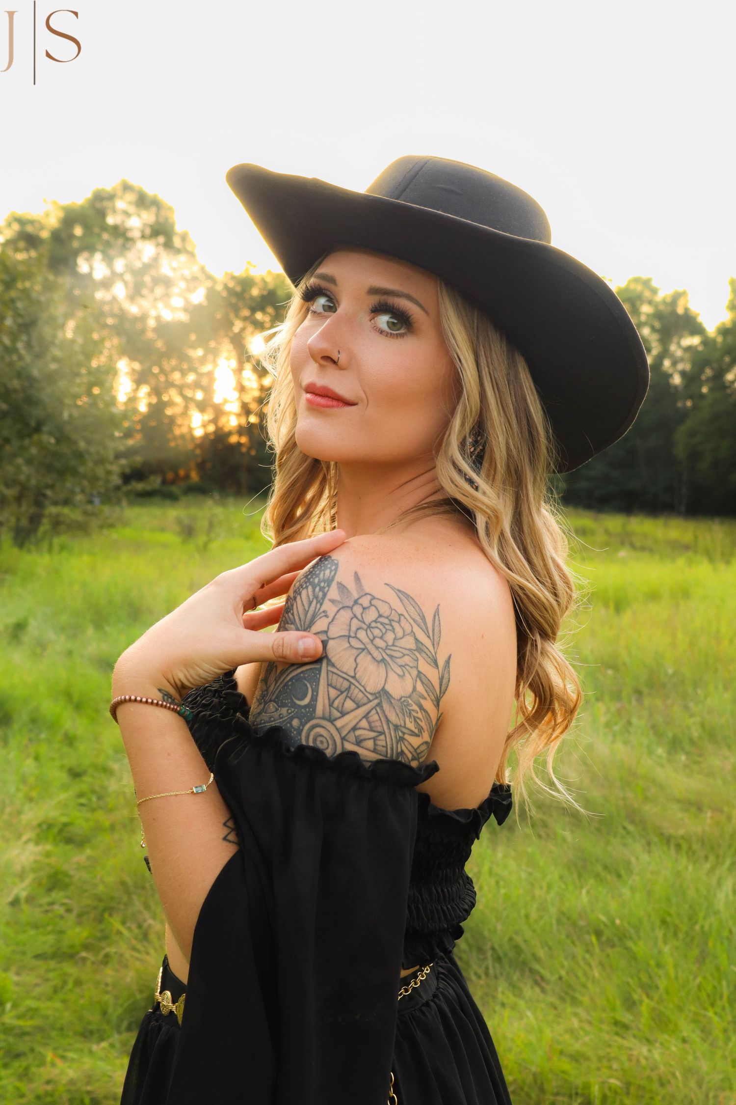 Outdoor photoshoot in a grassy field showing intricate back tattoo artwork and black dress.