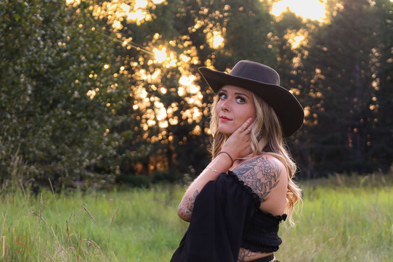 Silhouette of someone in a hat against golden sunset in grassy field.