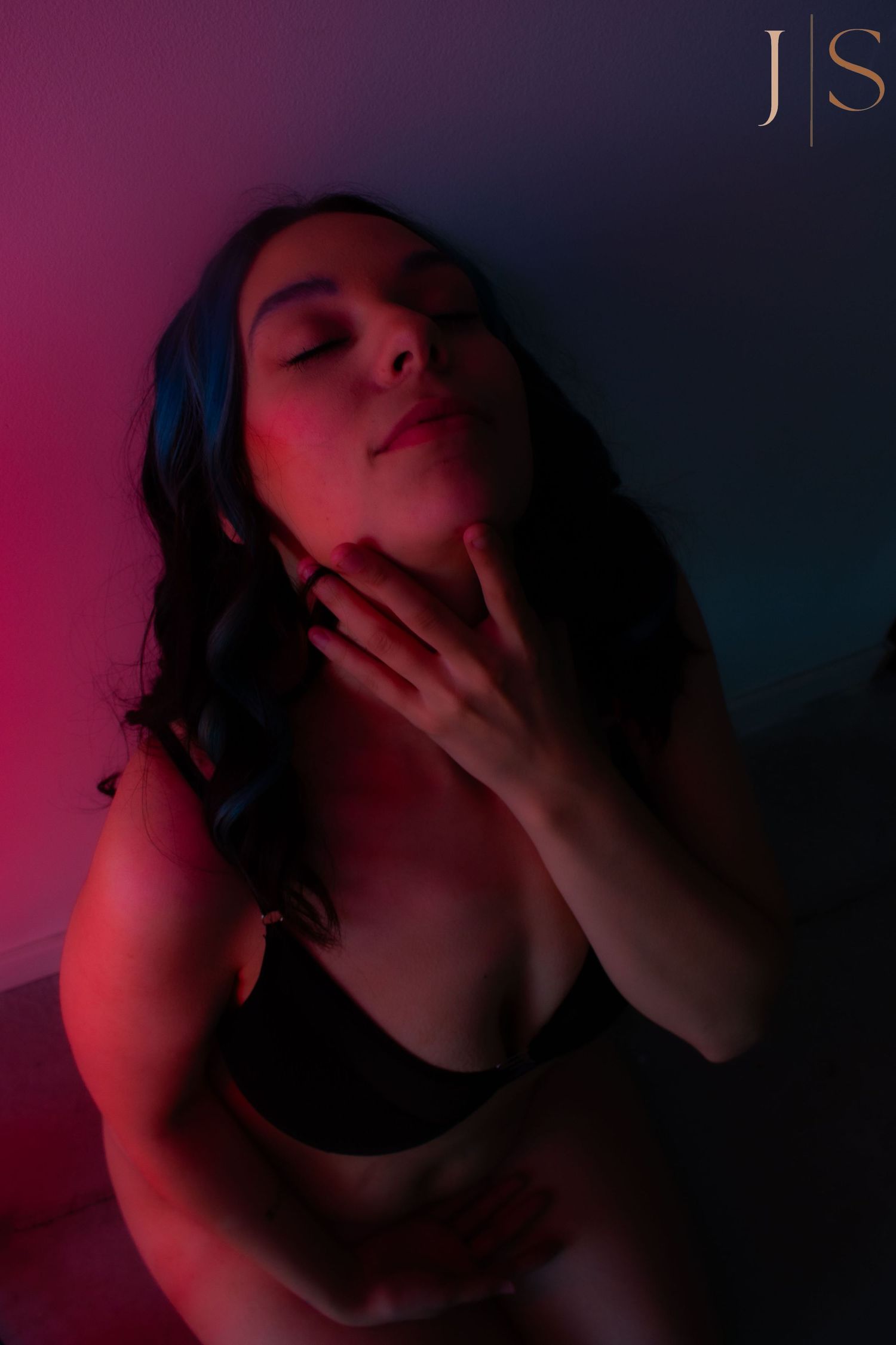 Moody boudoir portrait in dark room with red and blue lighting creating dramatic shadows and atmosphere.