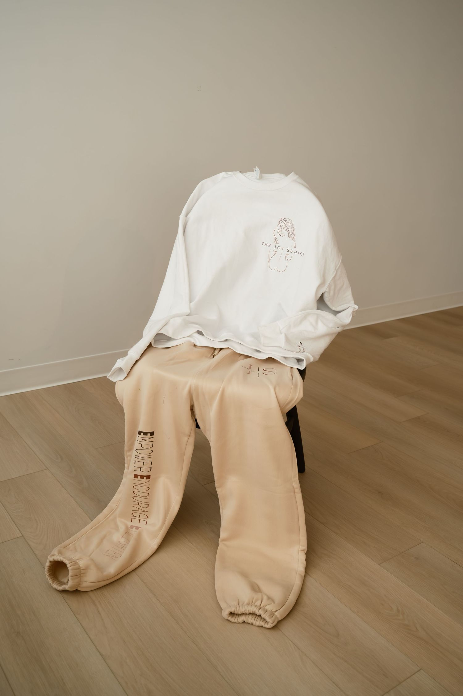 White long-sleeve shirt and beige sweatpants draped over a chair on light wood flooring against a neutral wall.