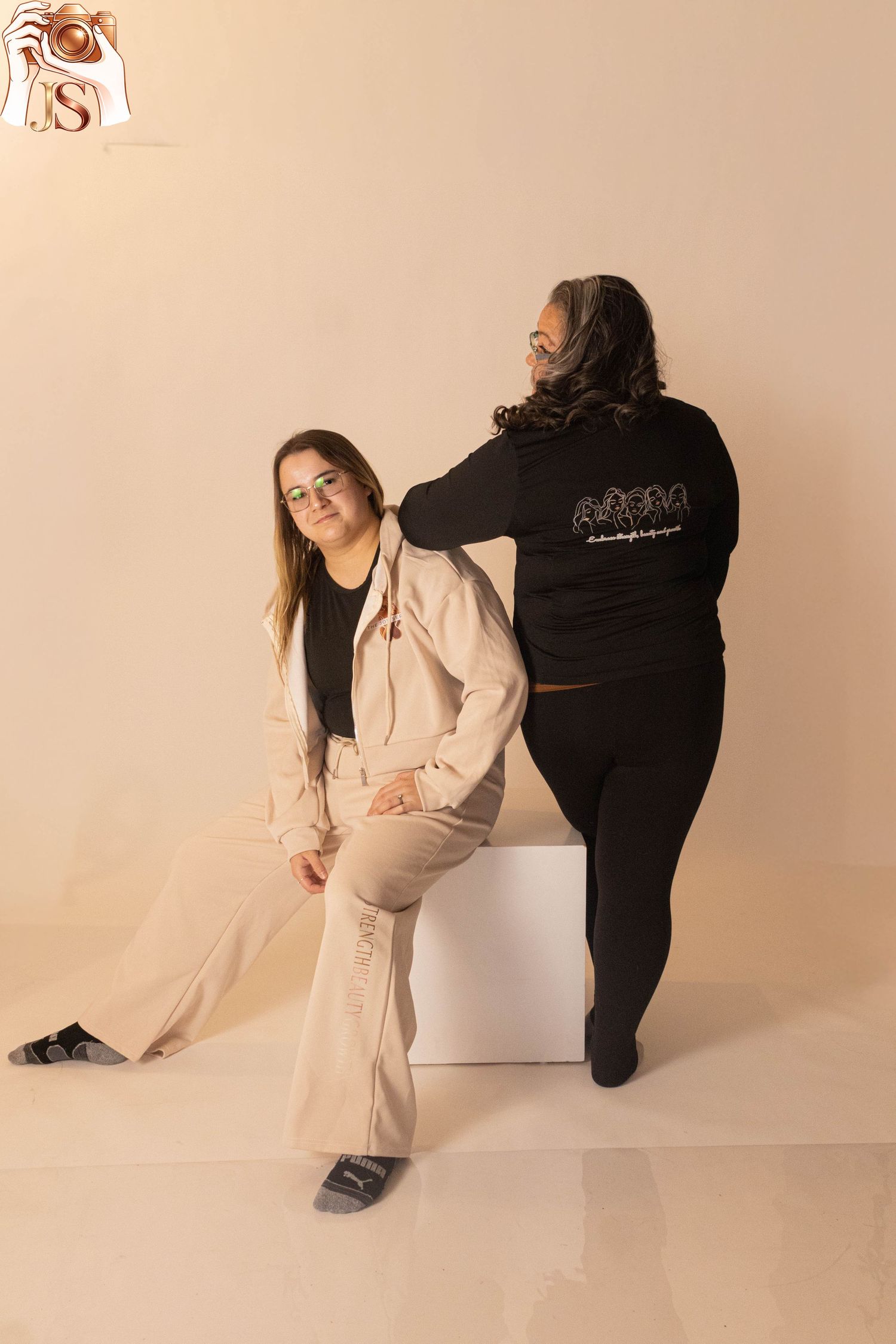 Two people in contrasting black and white outfits pose artistically against a beige studio backdrop in a photo series.