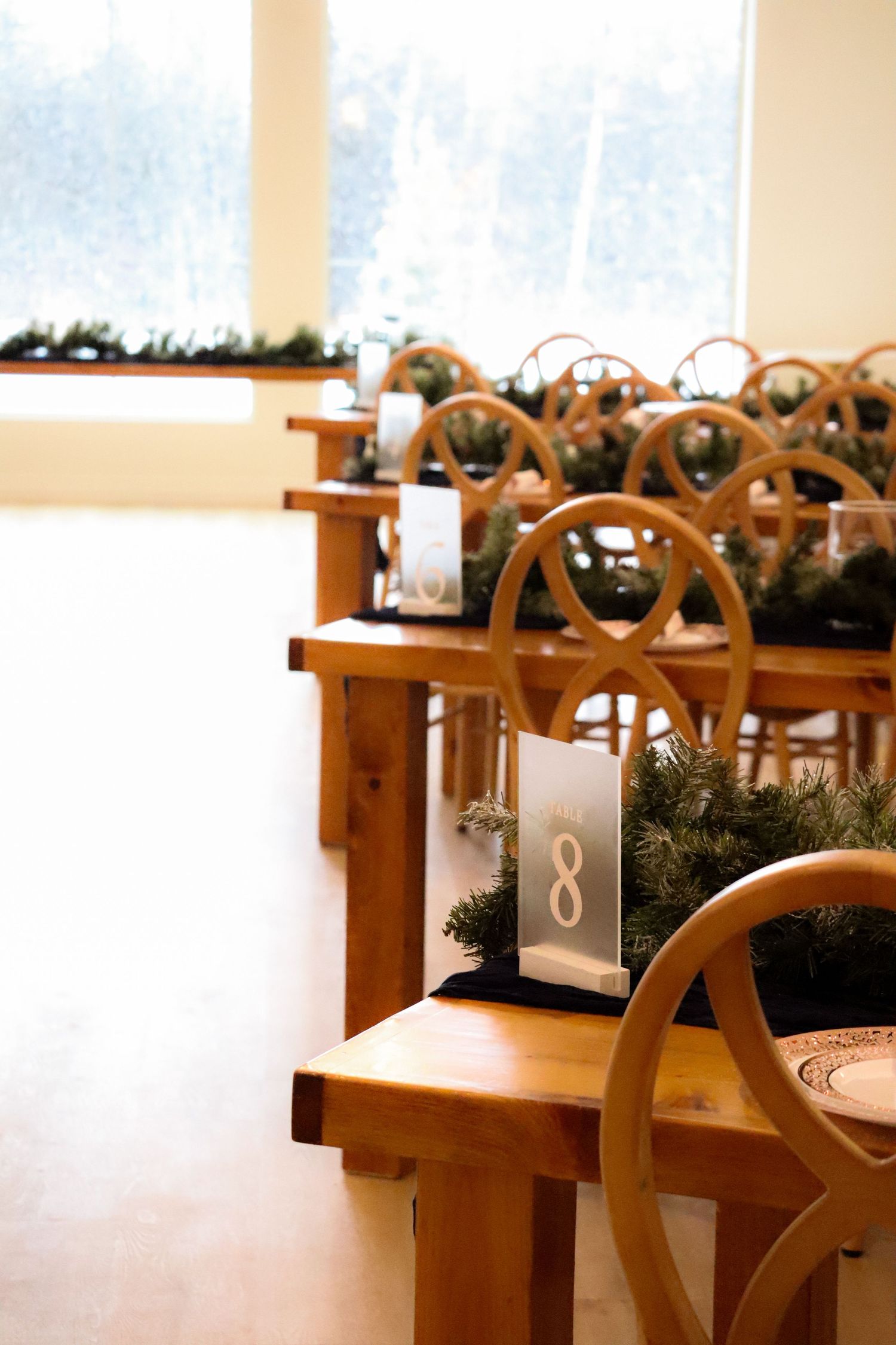 Wooden church pews decorated with evergreen garlands and lanterns in a bright ceremony space.
