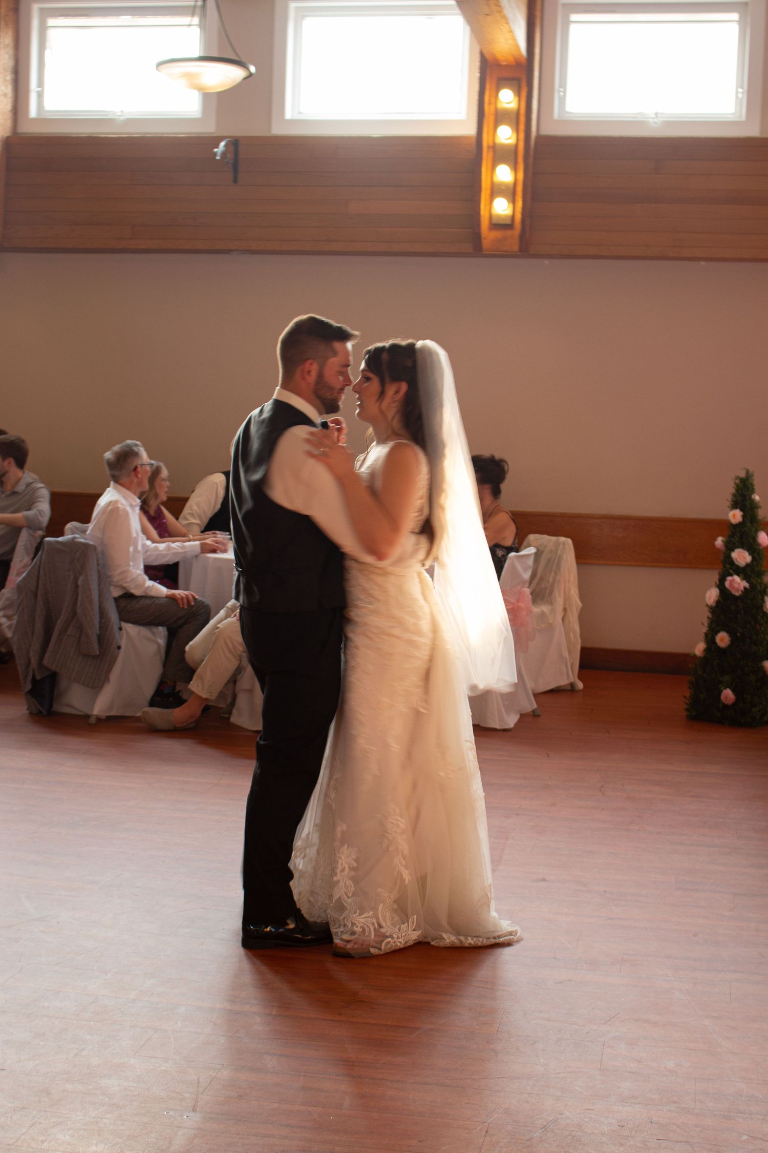 A couple shares their first dance at their wedding reception in a wooden-paneled venue.