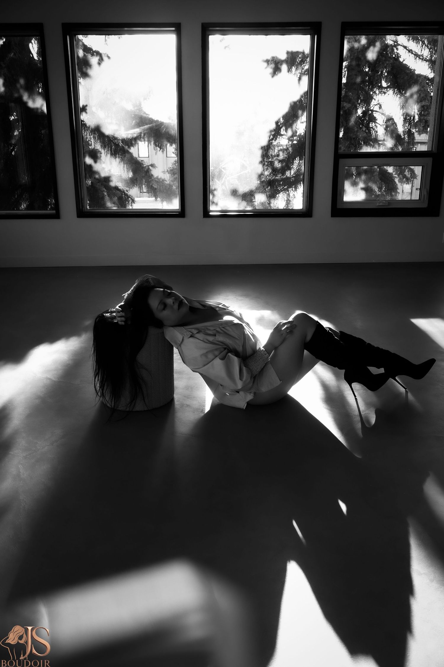 Black and white artistic photo of a figure reclining in dramatic window light on a hardwood floor.