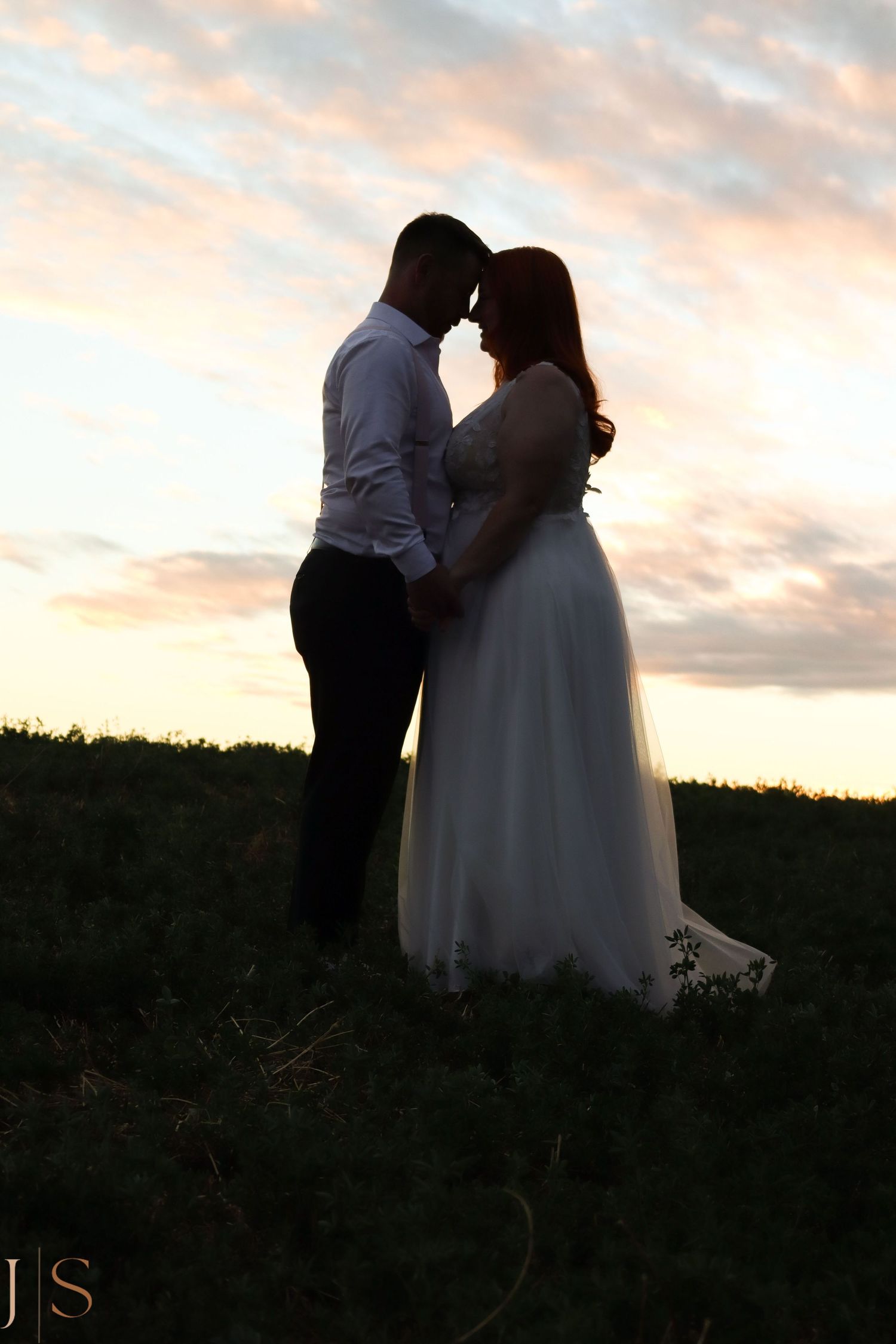 A couple shares a romantic moment silhouetted against a sunset sky during their wedding photoshoot.