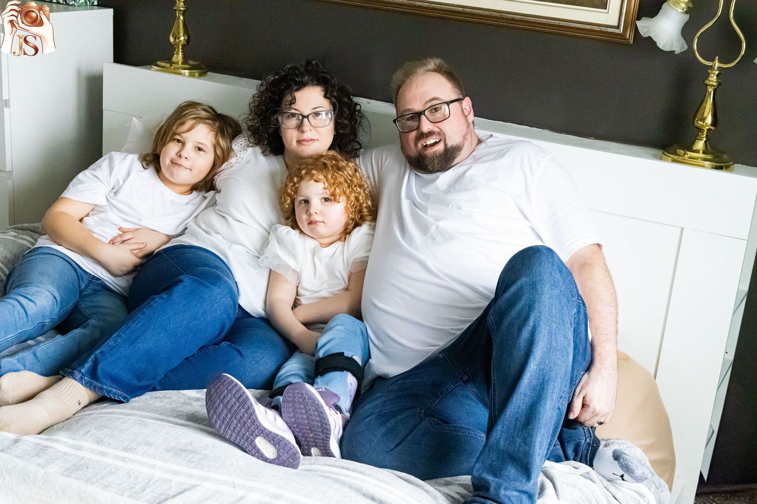 A family relaxes together on a white couch while reading a book at home.