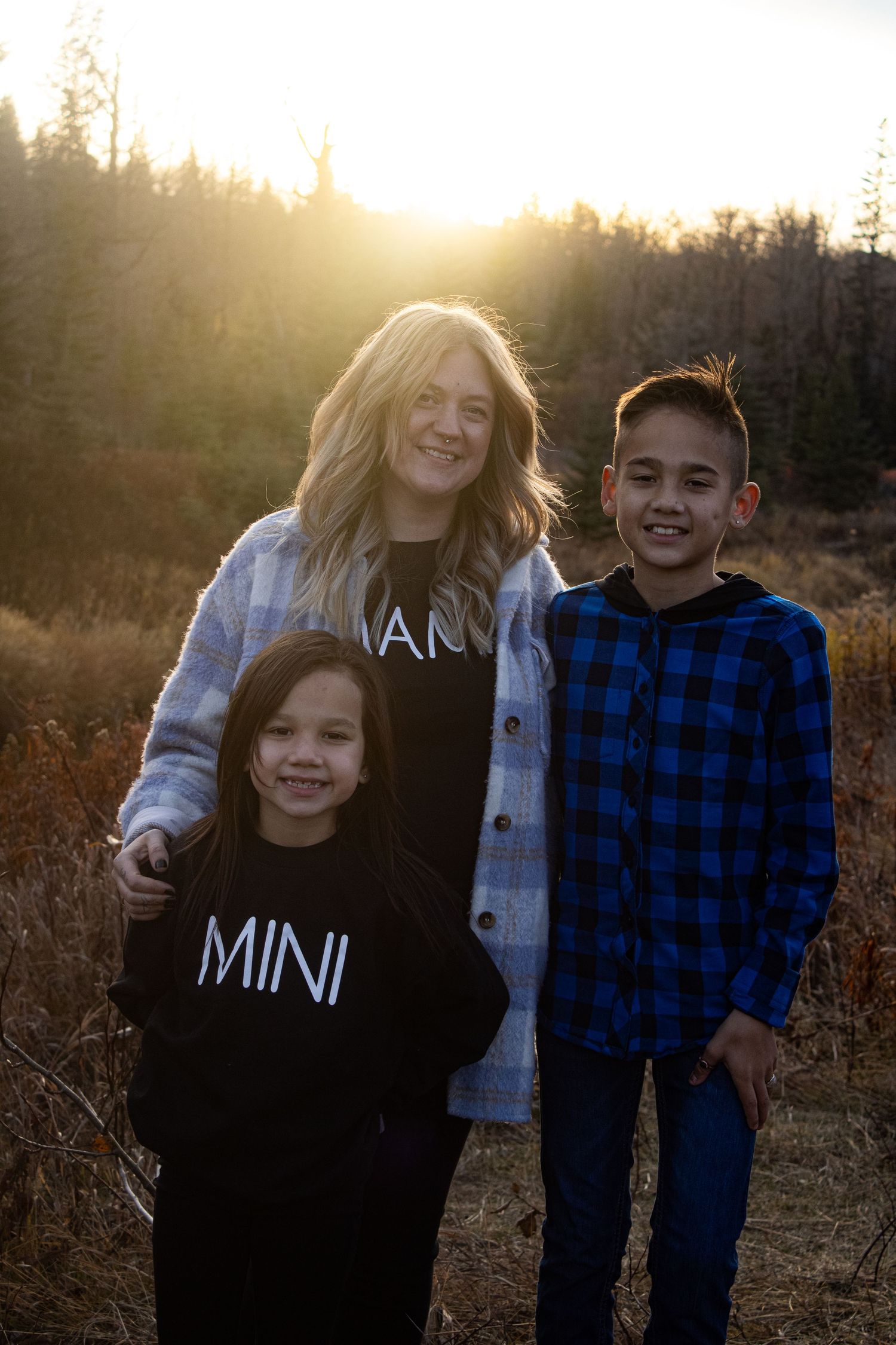 A family portrait at sunset with three people wearing casual clothes in a field.