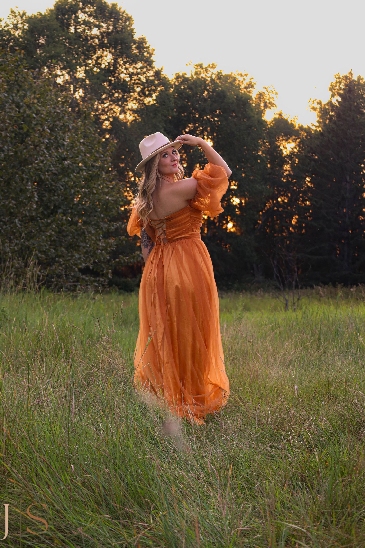 A figure in a flowing orange dress twirls gracefully in a sunlit meadow at golden hour.