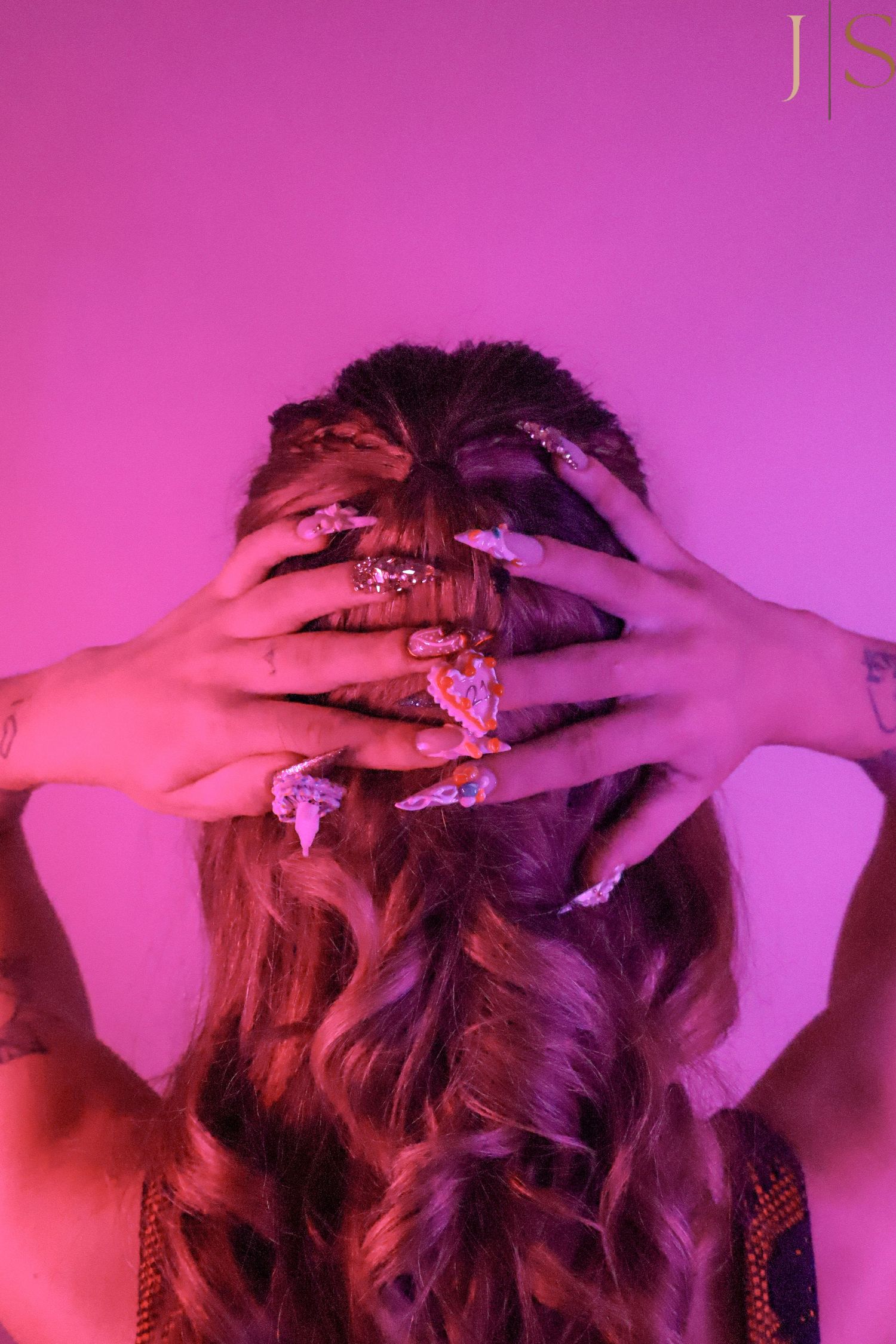 Multiple hands with pink manicured nails run through wavy hair against a magenta-colored background.