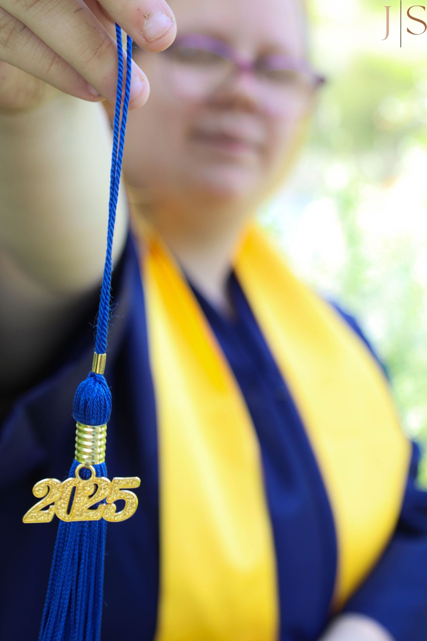 A blue and gold graduation tassel with 2025 charm dangles against a blurred background.