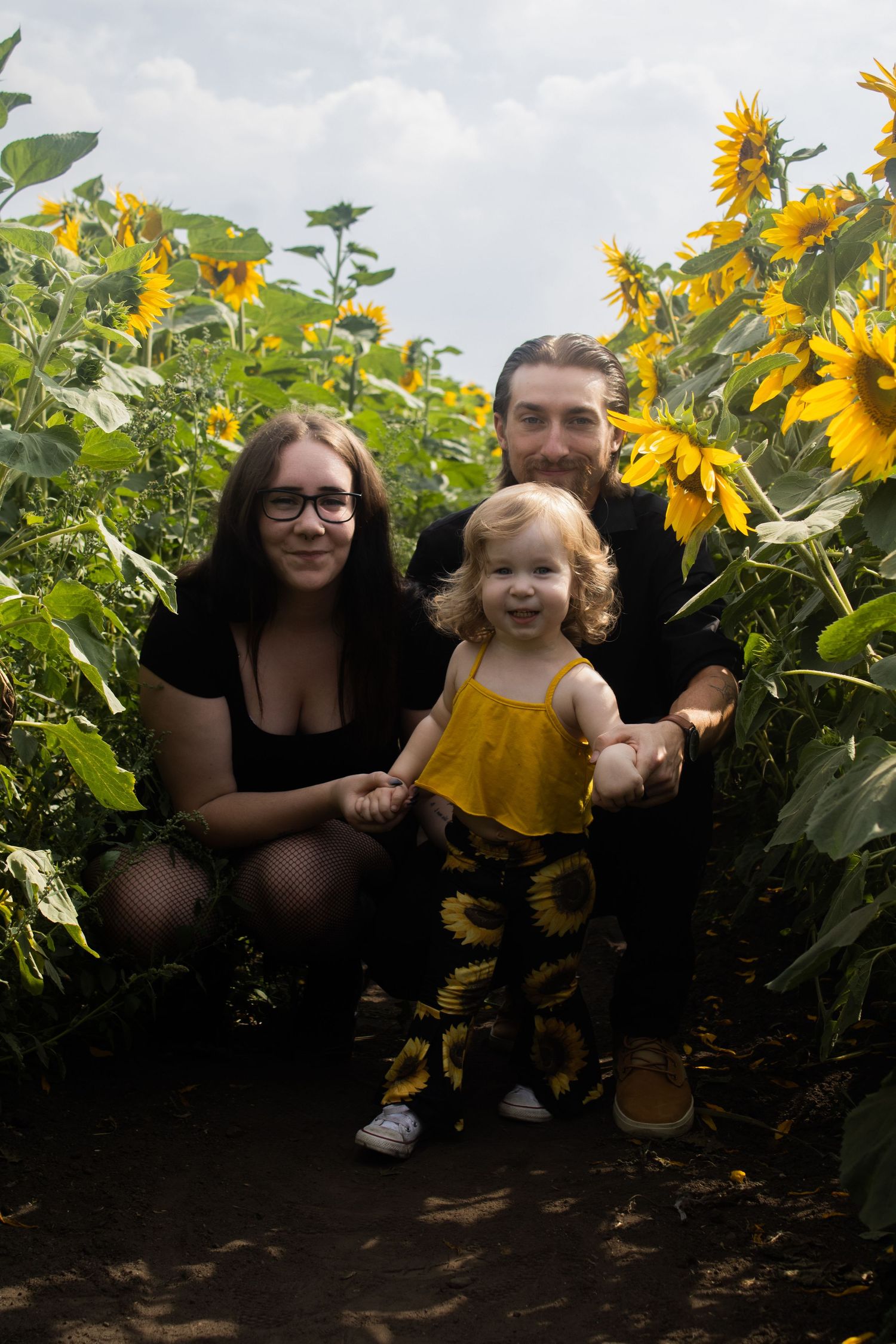 A cheerful family poses together in a vibrant sunflower field on a cloudy summer day.