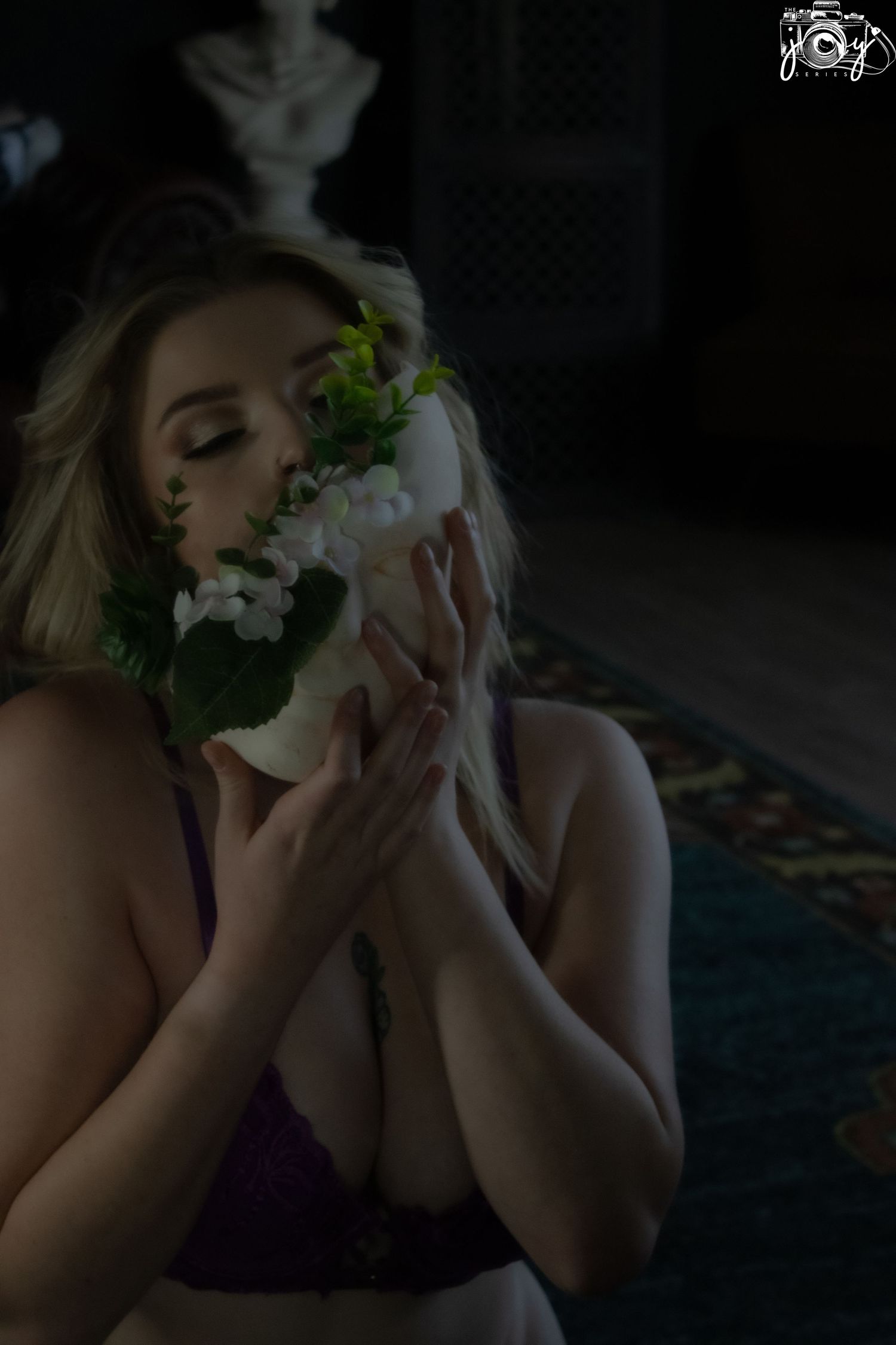 Dark atmospheric portrait in purple lingerie holding white flowers with moody lighting and shadows.