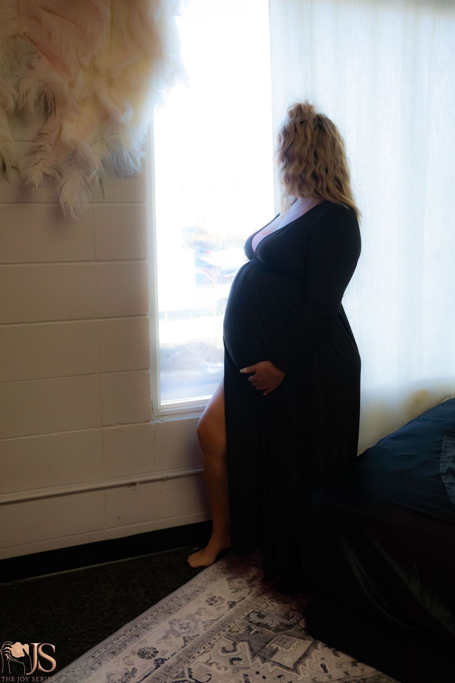 A silhouetted side view of a pregnant woman in a black dress standing by a window in soft lighting.