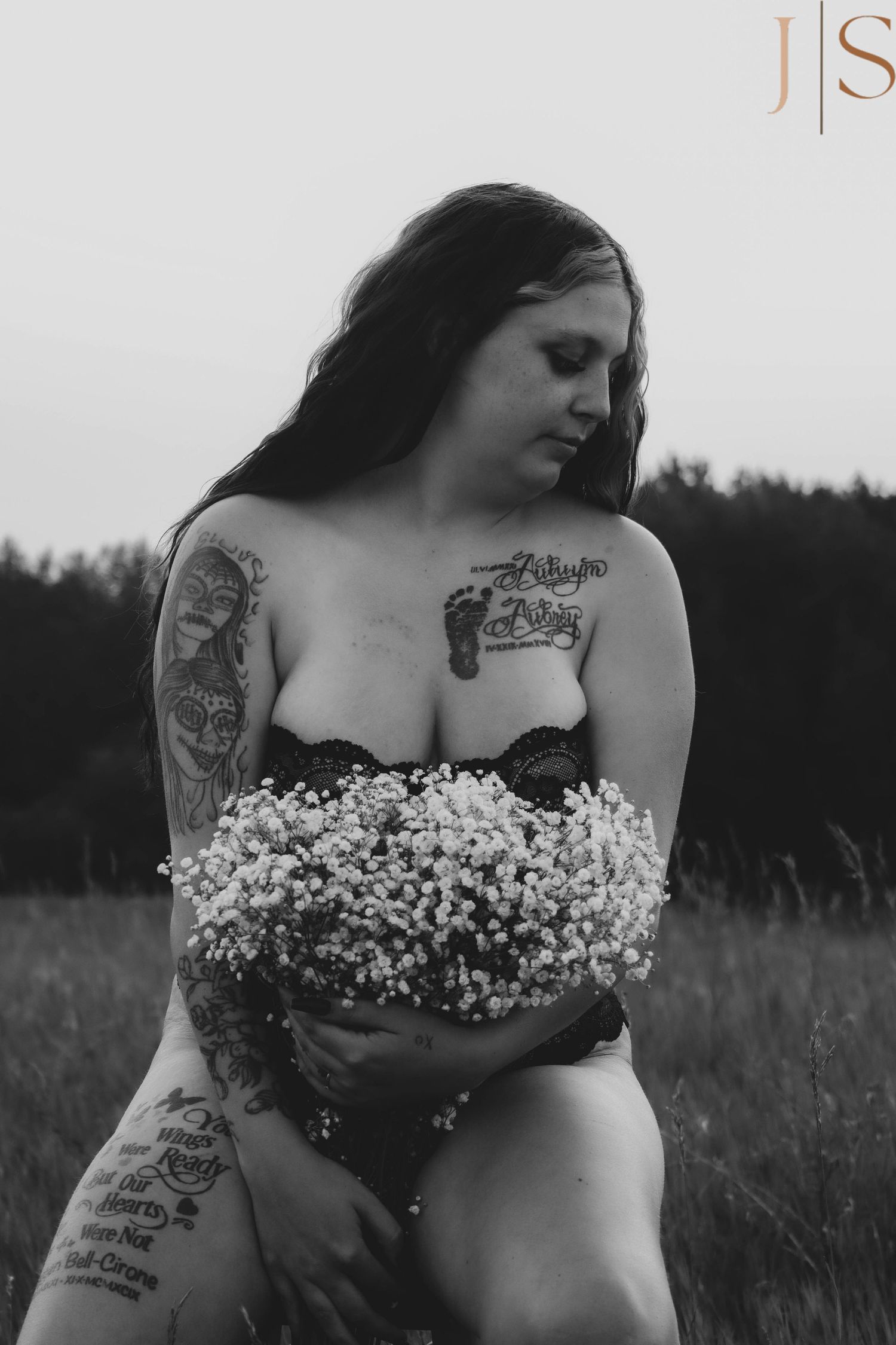 Artistic black and white photo of a tattooed figure in nature holding delicate baby's breath flowers.