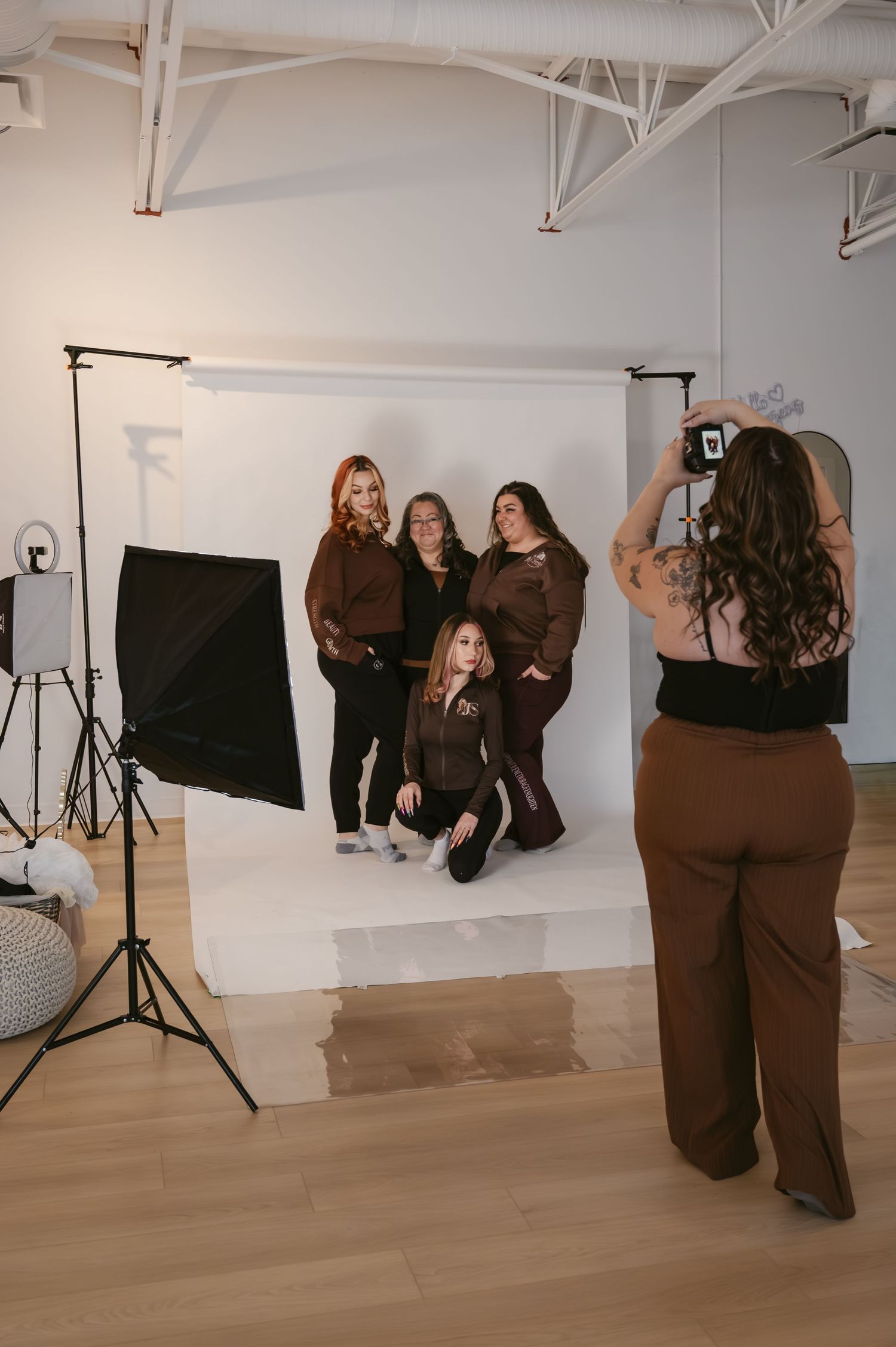 Photographer captures four women in brown outfits posing in front of white backdrop in professional photo studio.