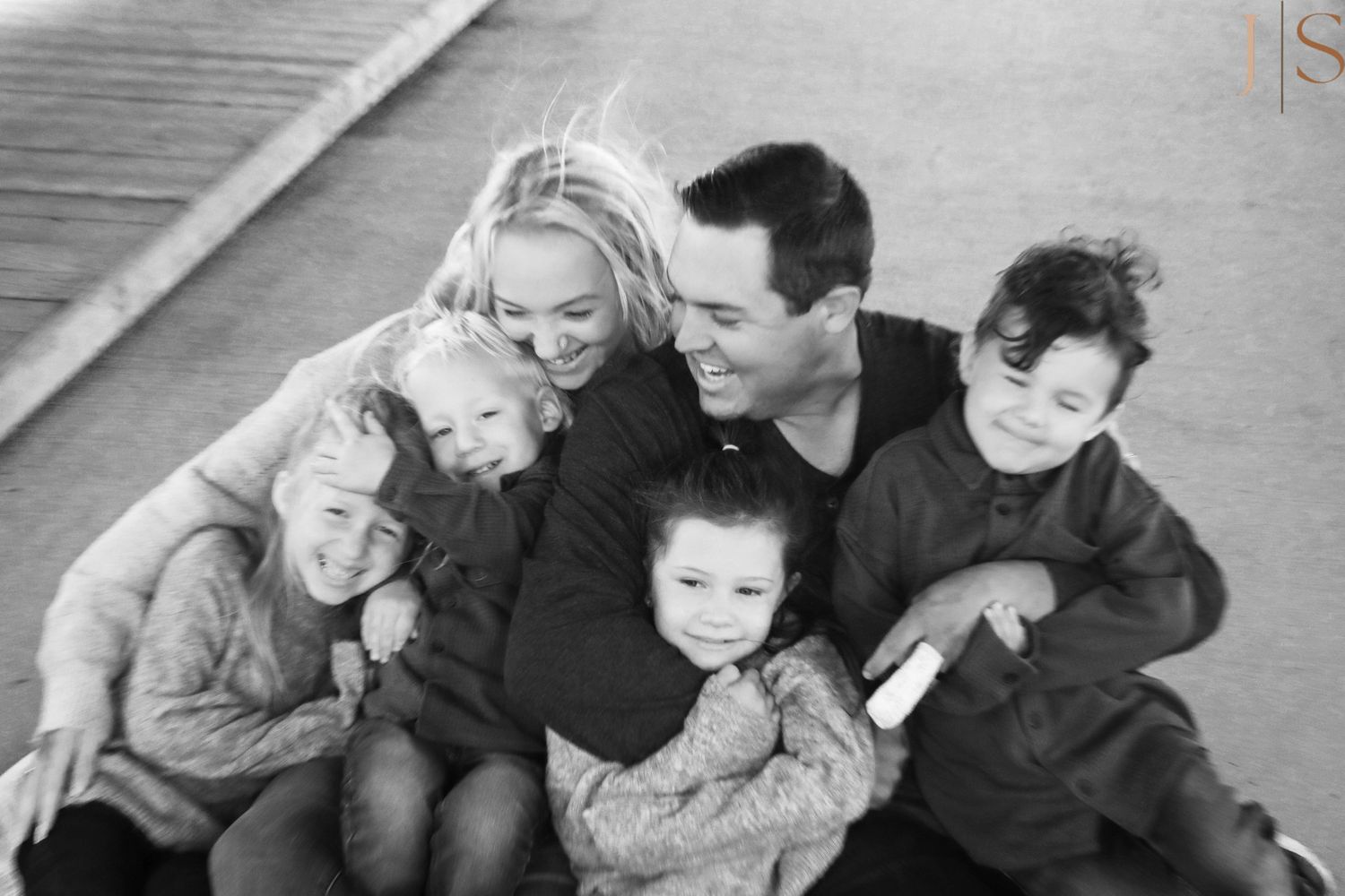 A black and white candid family portrait showing parents and three children laughing together on wooden steps.