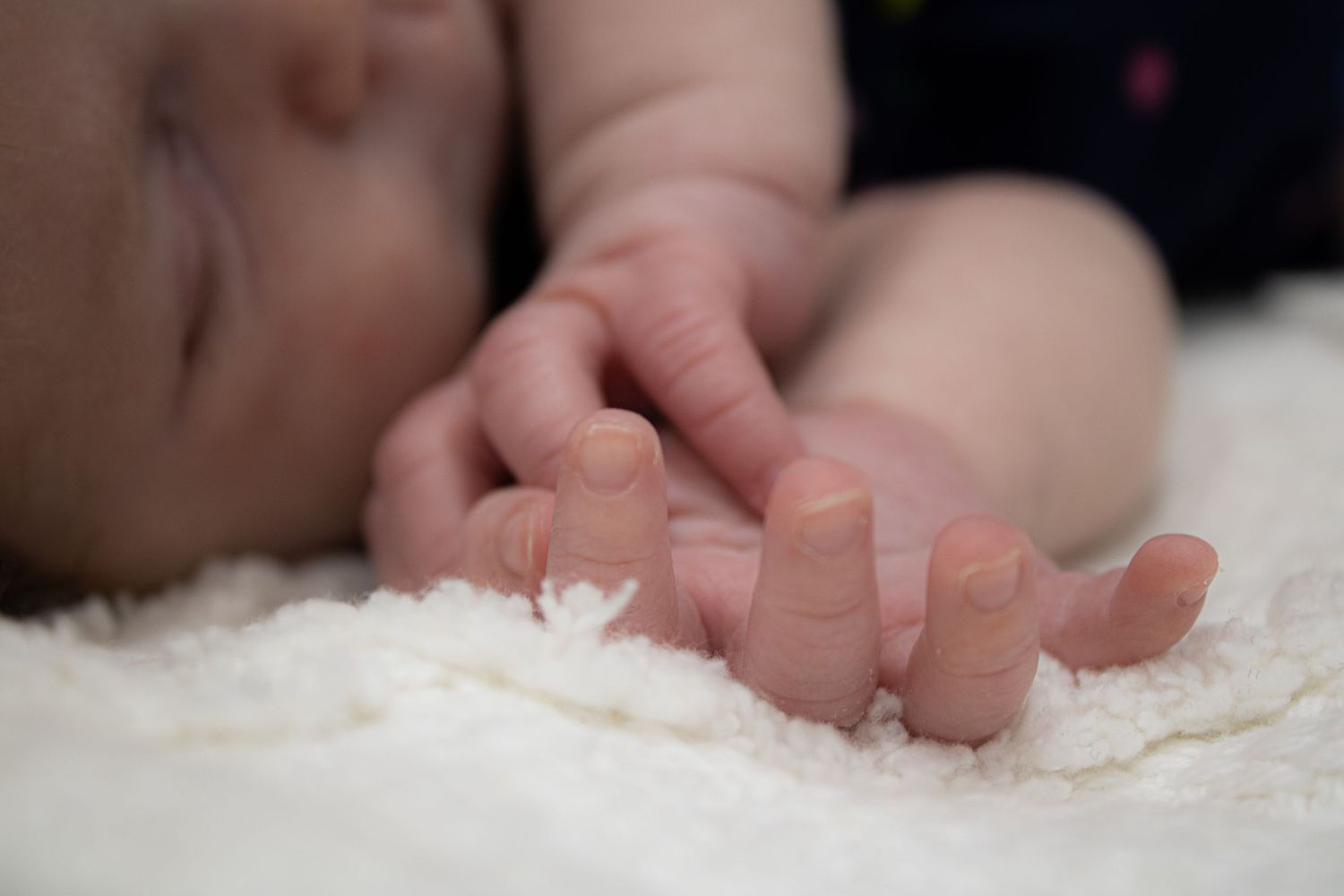 Close-up of a baby's tiny hand resting on soft white fabric.