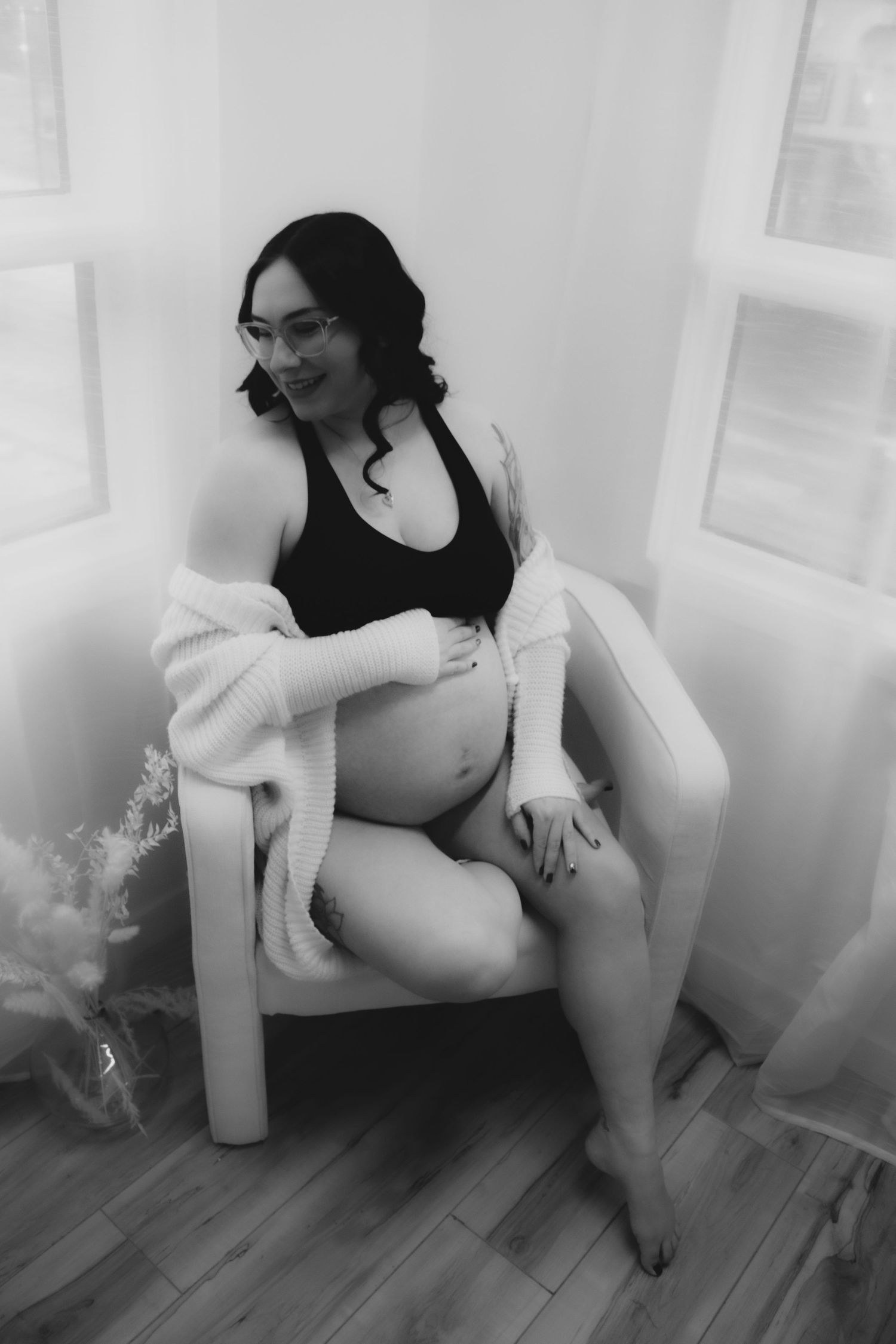 Maternity photo of expectant mother relaxing in white chair by window.