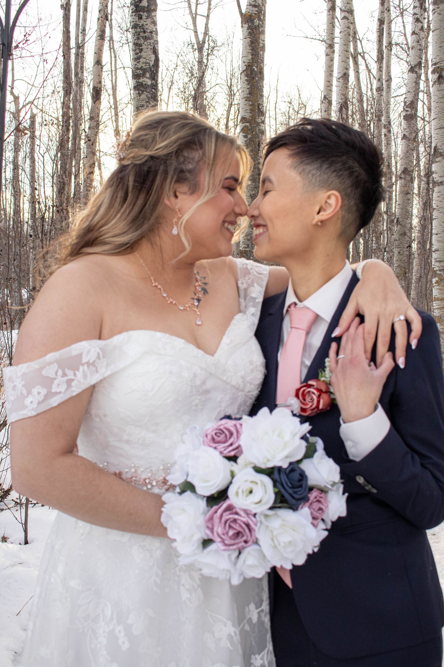 Winter wedding portrait with a loving couple holding a bouquet of white and pink roses.