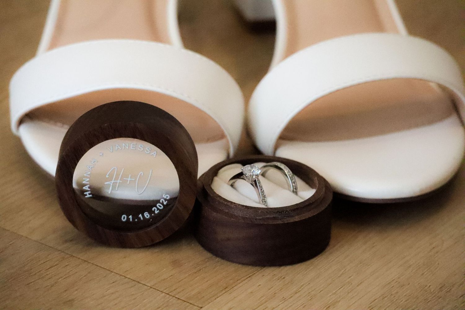 White bridal shoes next to wooden ring boxes on hardwood floor.
