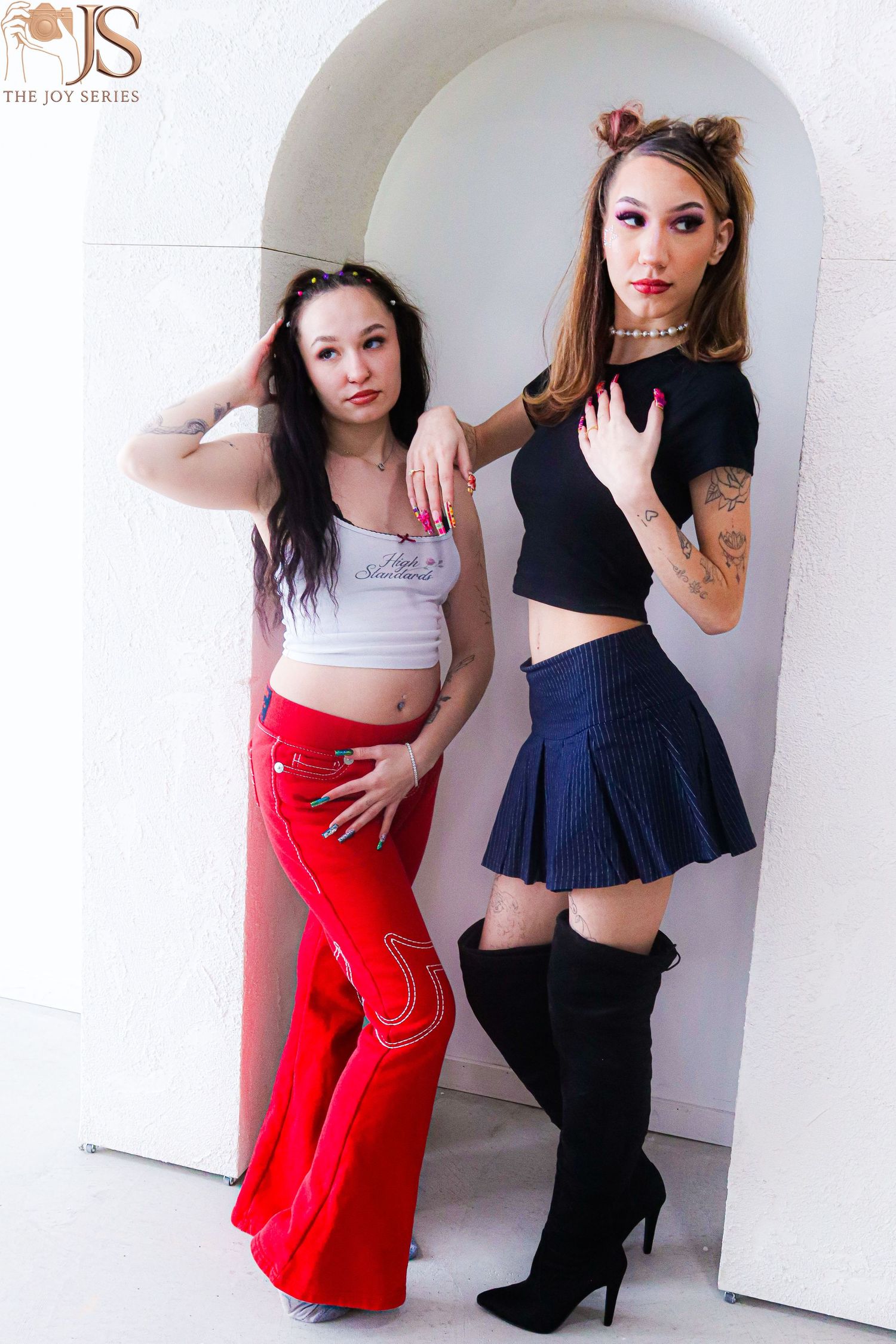 Fashion duo posing in contrasting outfits against white studio backdrop.