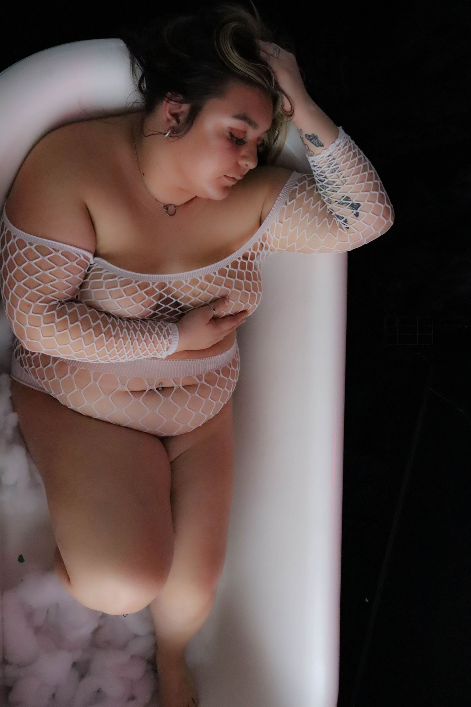 Artistic boudoir photo showcasing netted white lingerie against dark background in moody lighting.