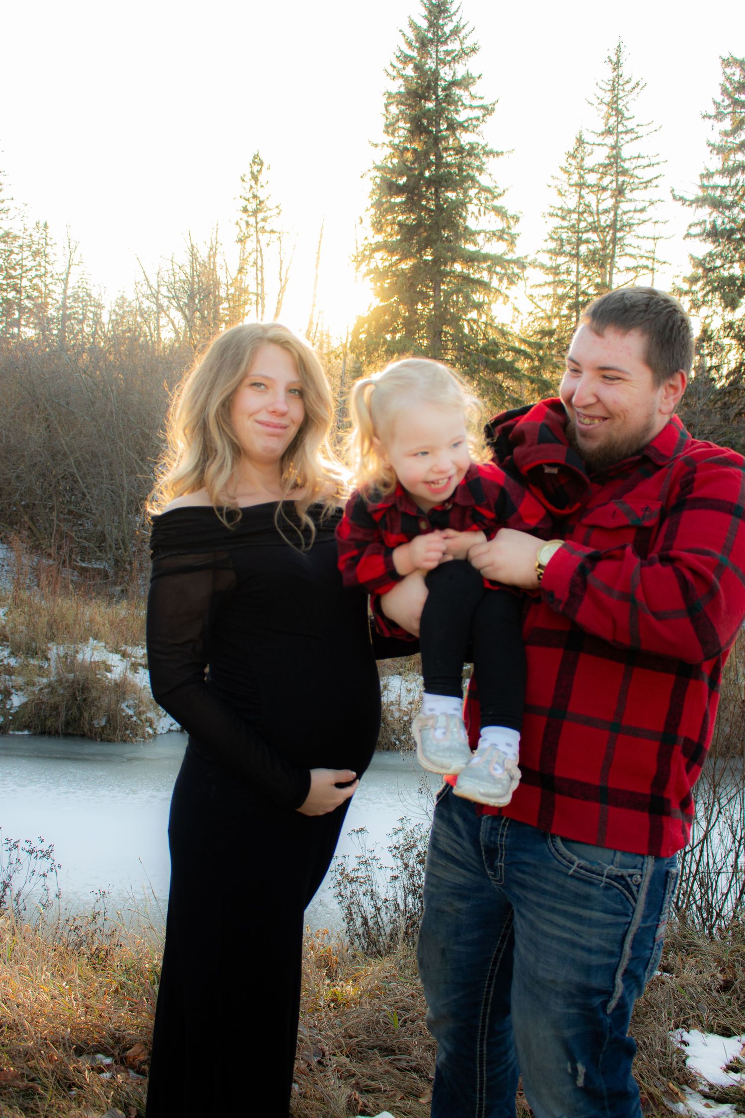 Winter family portrait with matching red plaid outfits against snowy forest backdrop.