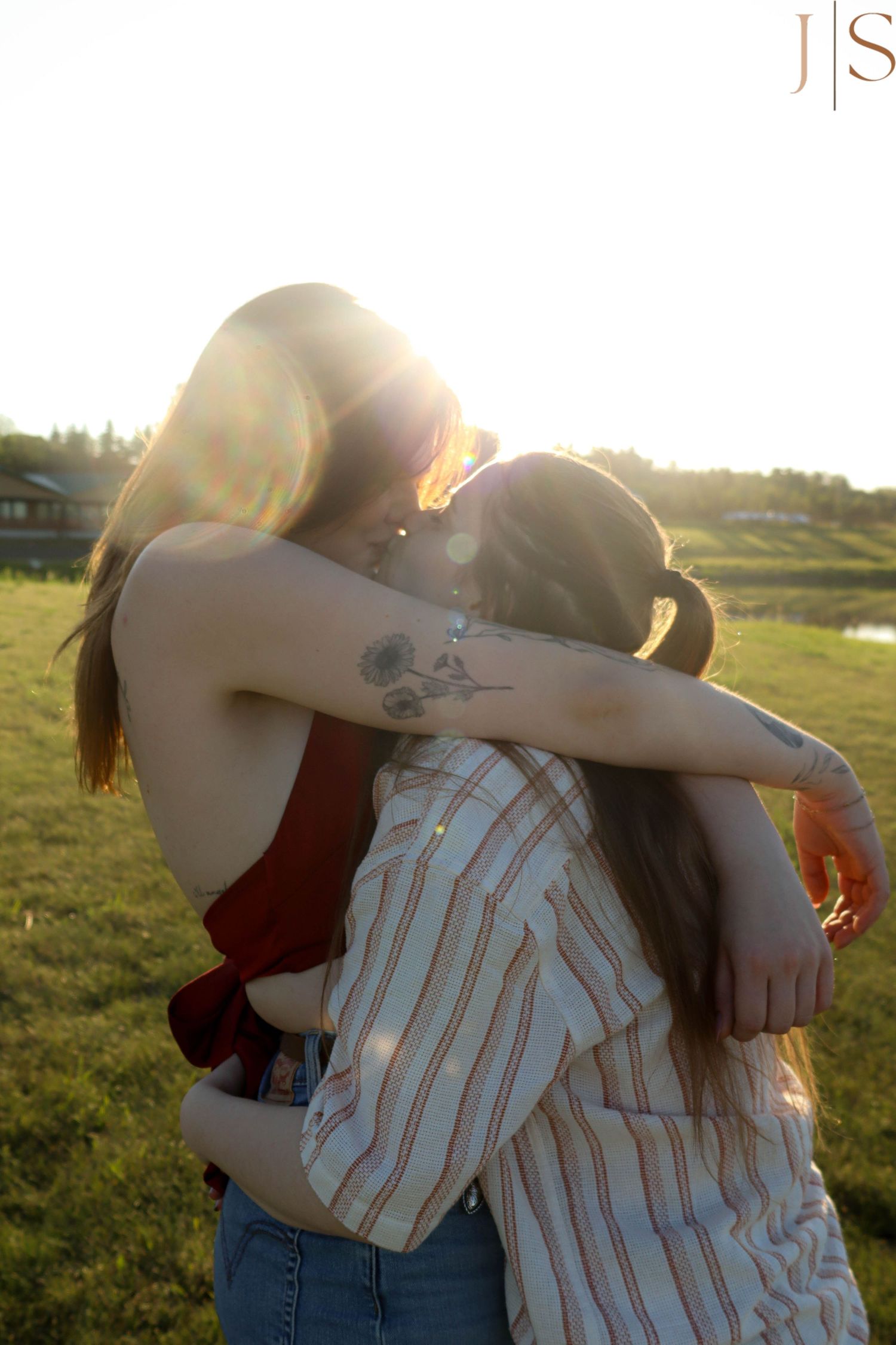 Two people embrace in a warm hug outdoors during golden hour sunlight in a grassy field.