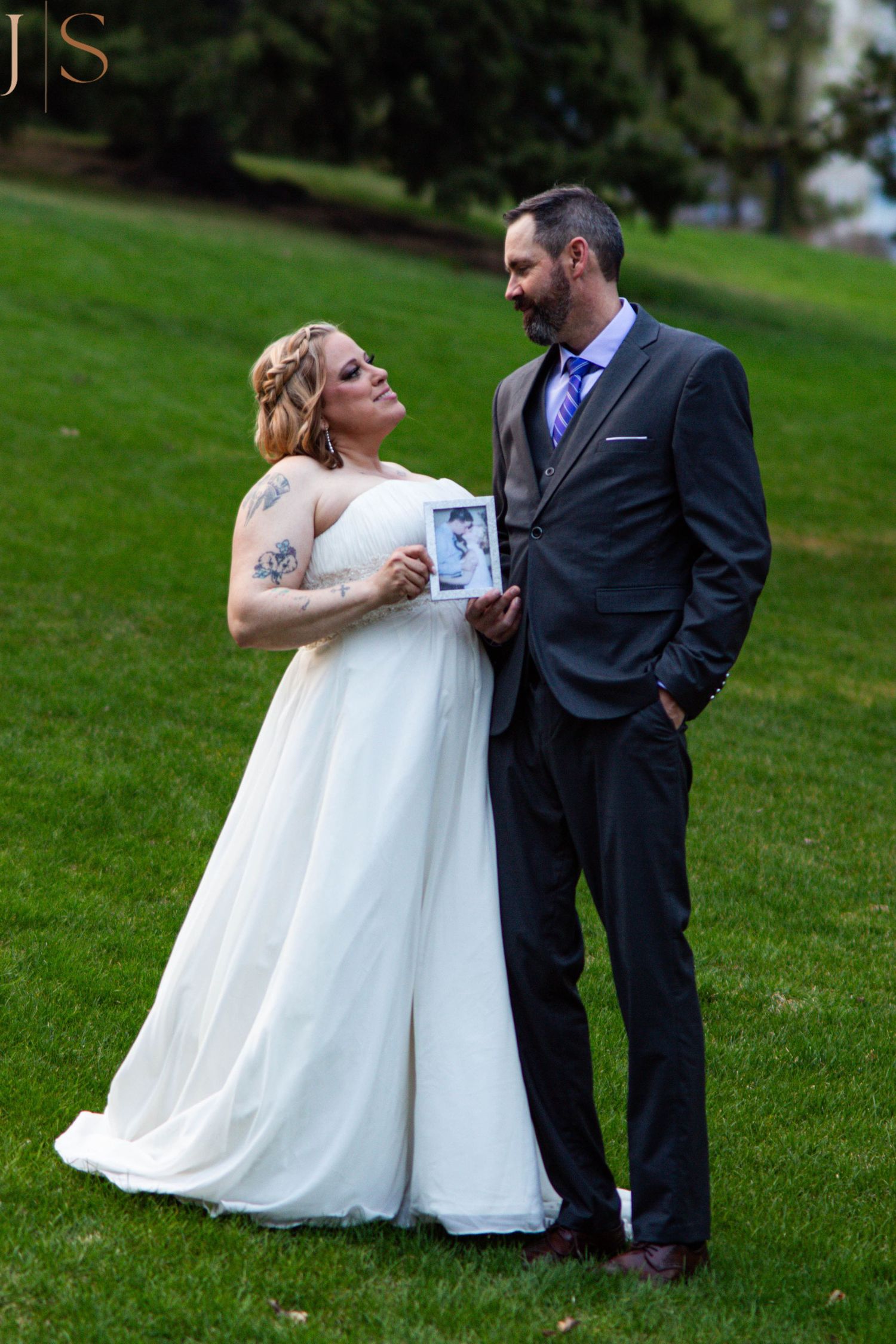 Wedding couple poses together on grassy hill during outdoor photography session.