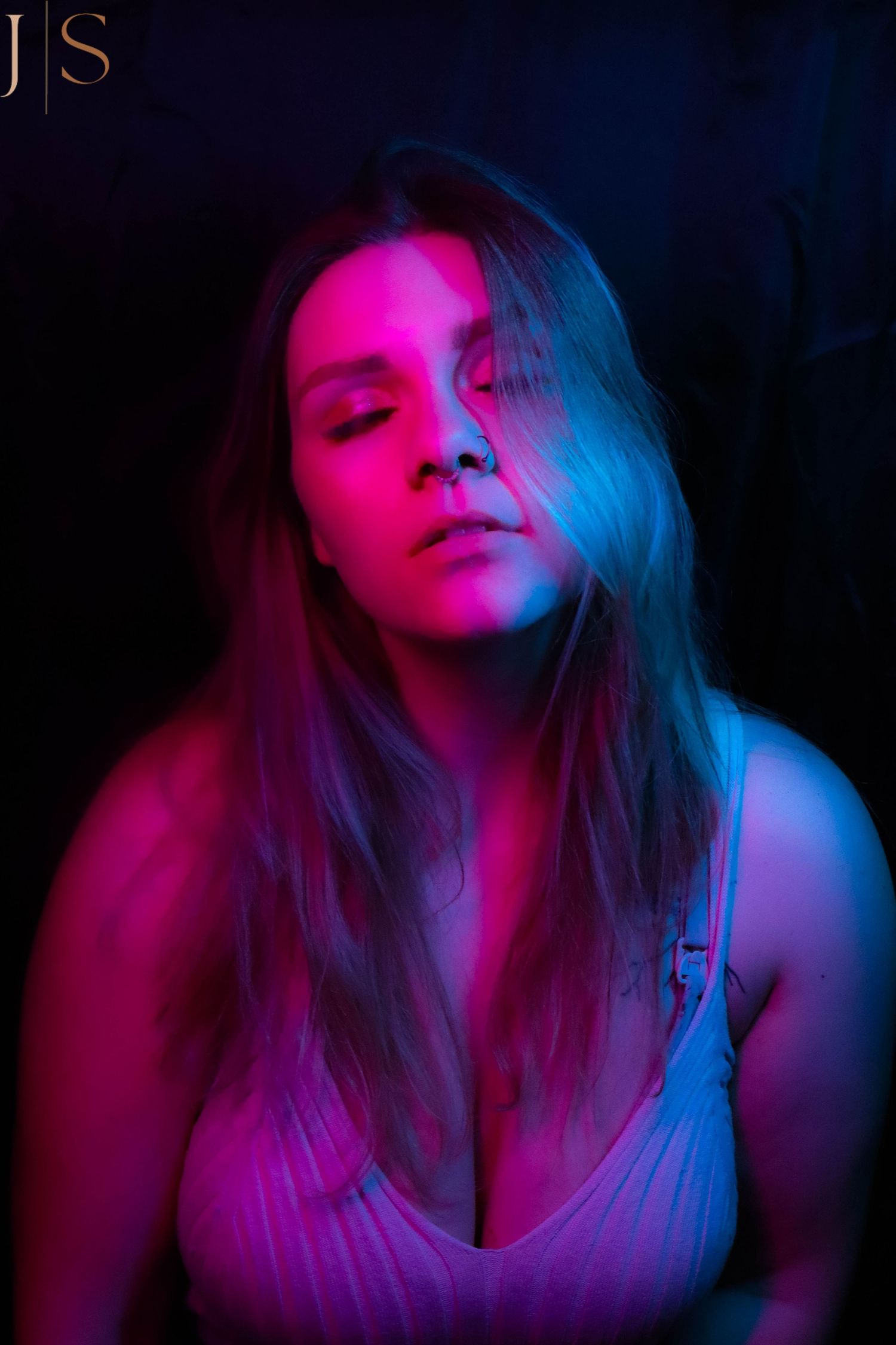 Artistic portrait with dramatic neon pink and blue lighting creating a moody atmosphere against dark background.