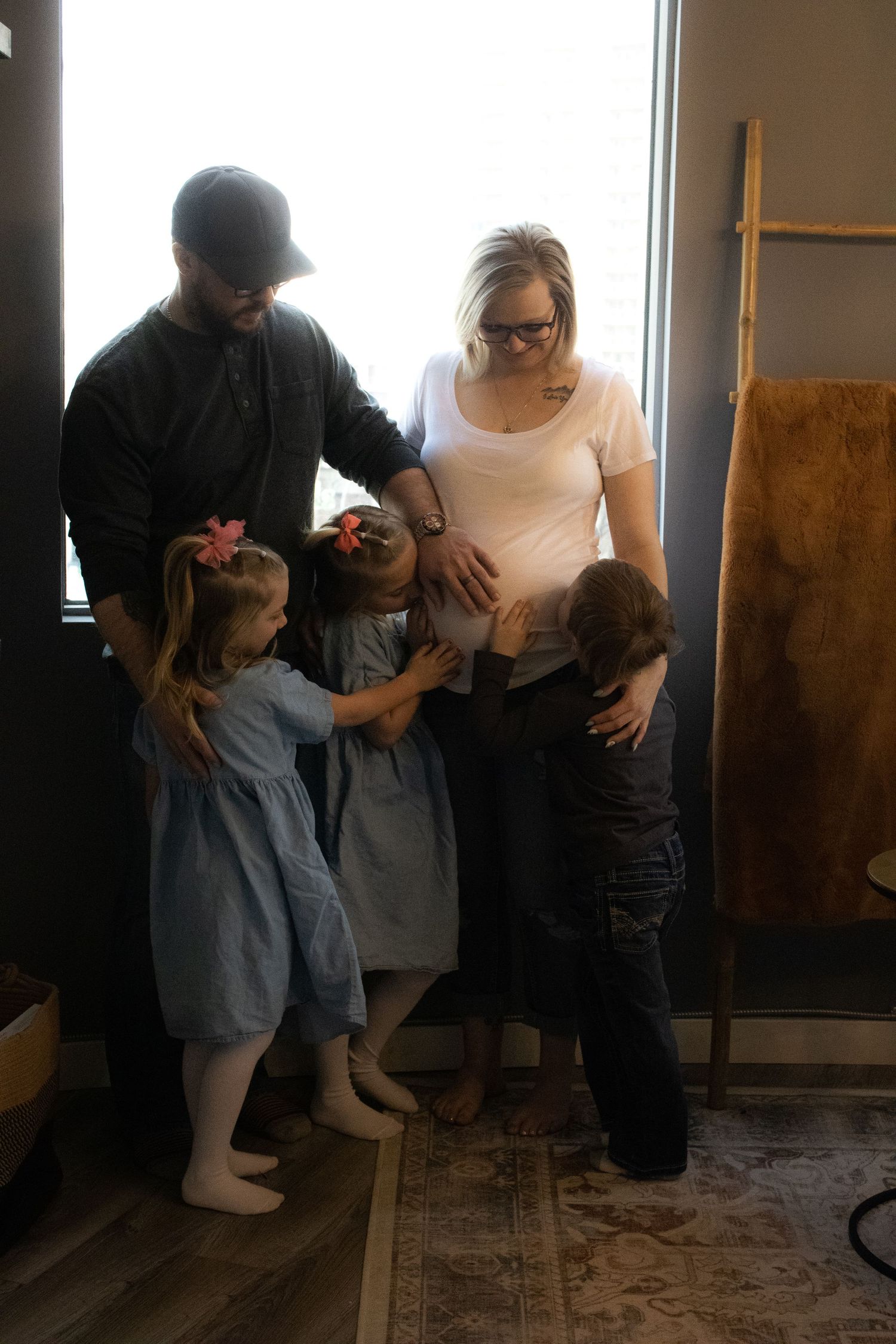 A family gathering shows parents and children sharing an intimate moment by a window.