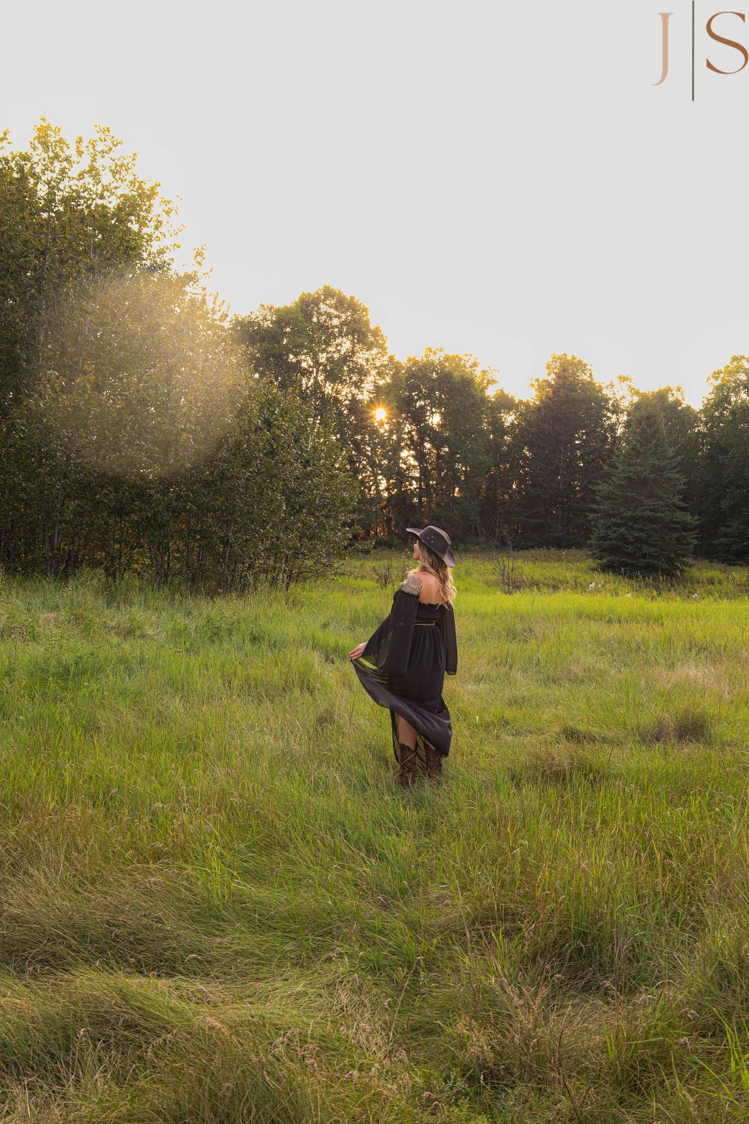 Person walking through a sunlit meadow with tall grass and trees in the background during golden hour.