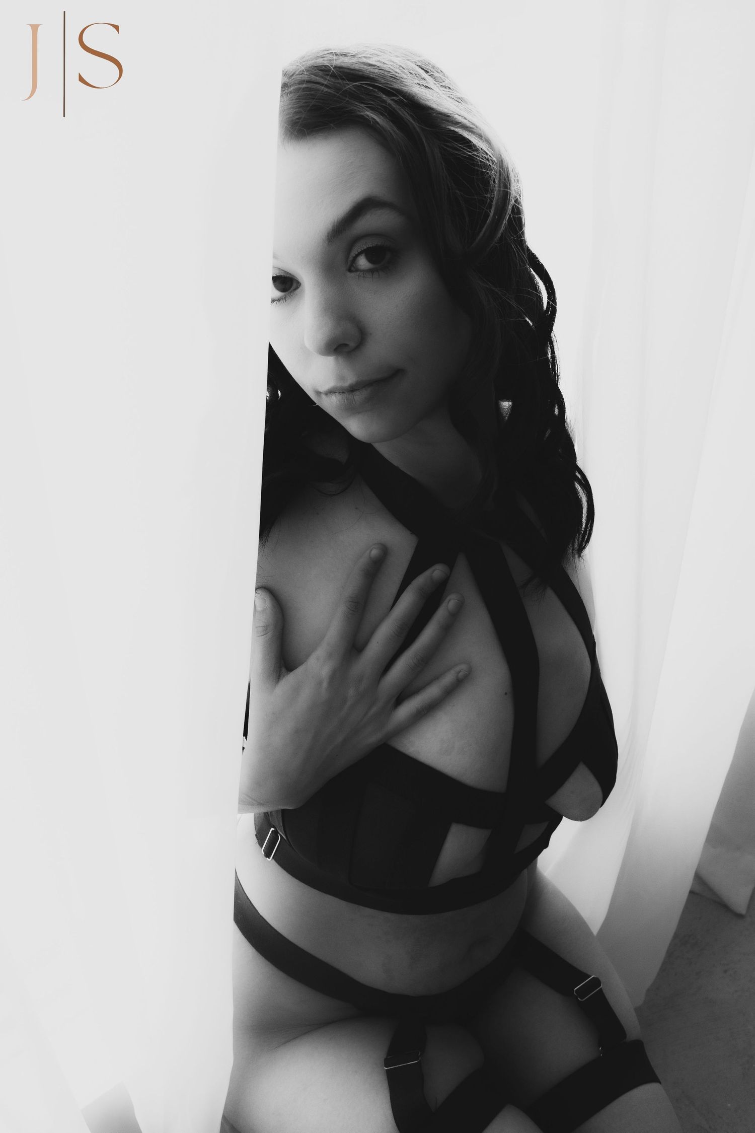 Black and white artistic boudoir portrait showing a woman in lingerie posing against a light wall.
