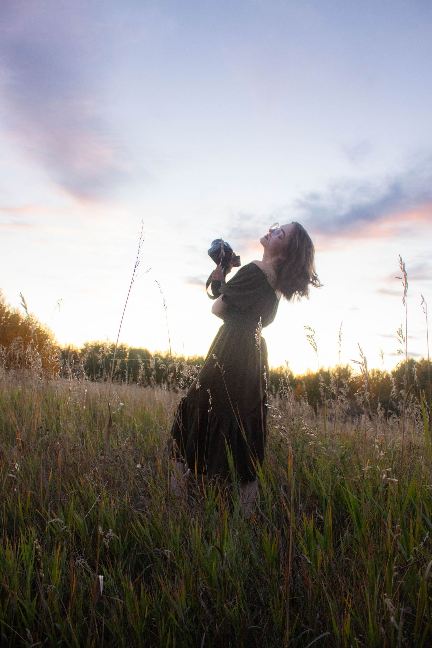 Artistic silhouette portrait of photographer holding camera in golden field at dusk.