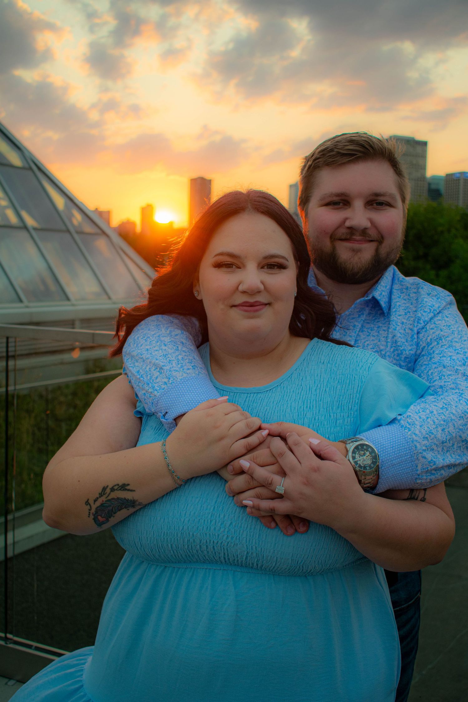 Couple sharing tender moment at sunset with glass pyramid architecture in background.