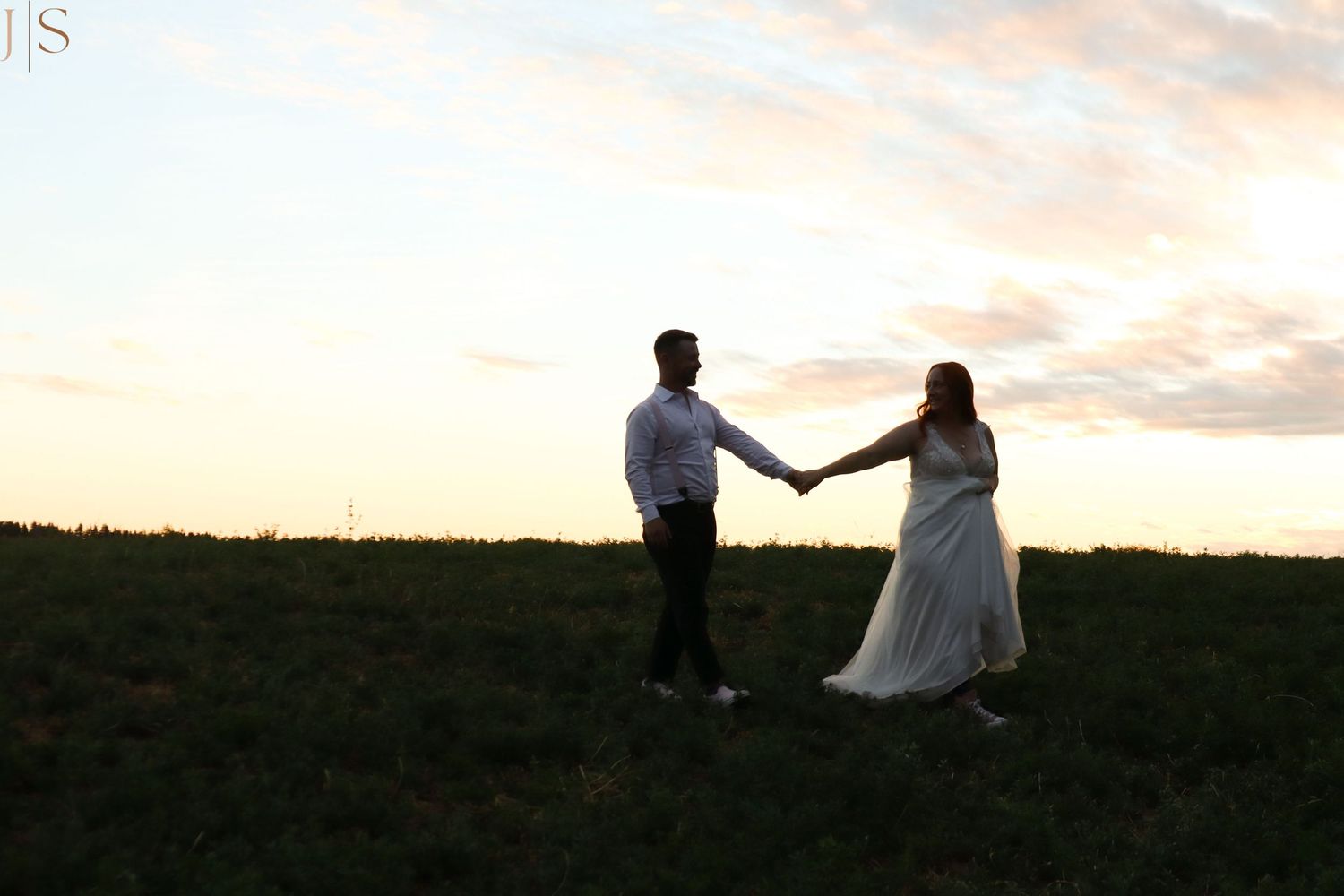 A couple sits together on a grassy hilltop at sunset enjoying a romantic moment.