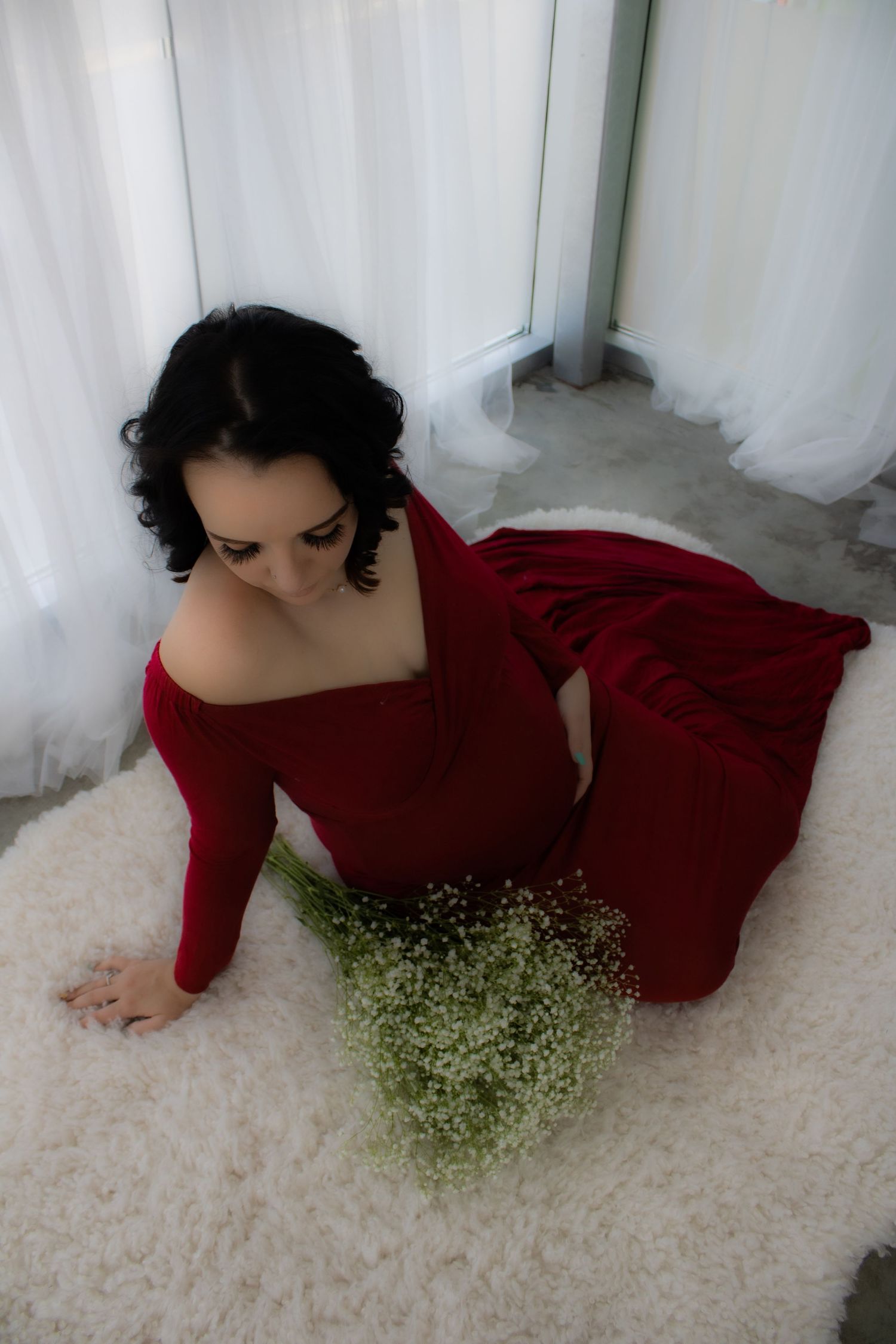 A dramatic maternity photo with a woman in red velvet dress sitting with baby's breath flowers.