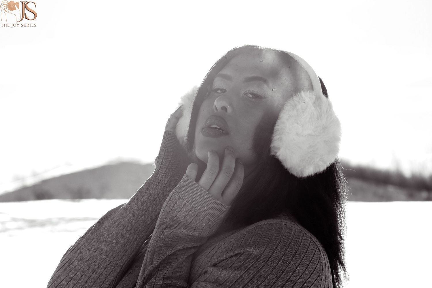 Black and white winter portrait of person wearing fuzzy earmuffs outdoors.