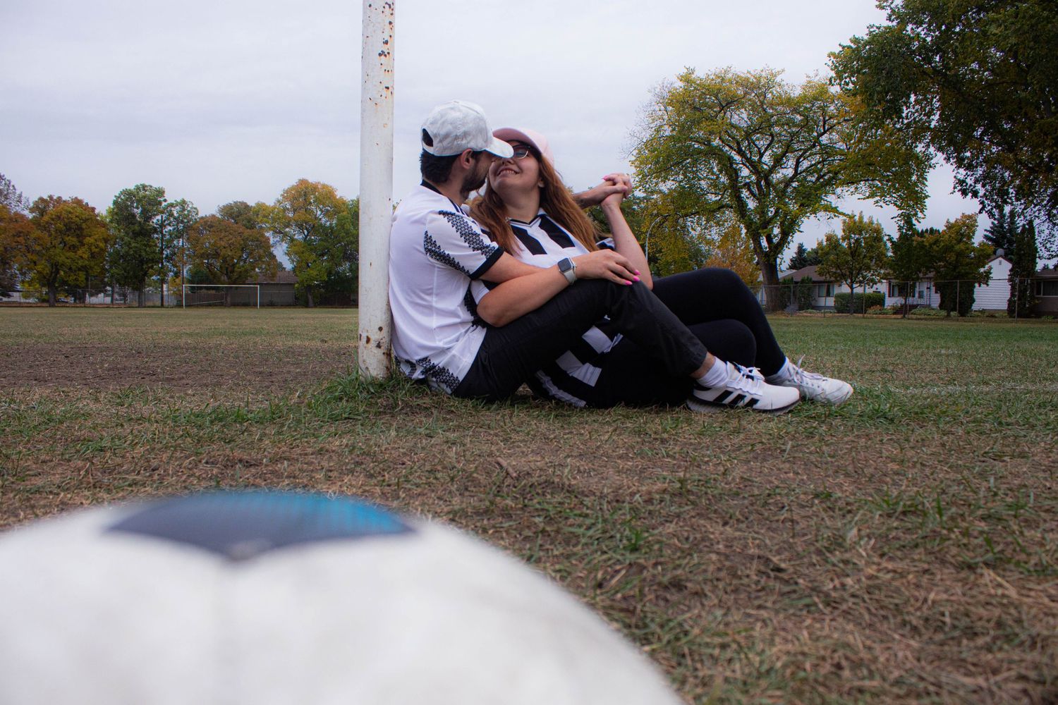 Couple relaxing on grass in a park with autumn trees in background.