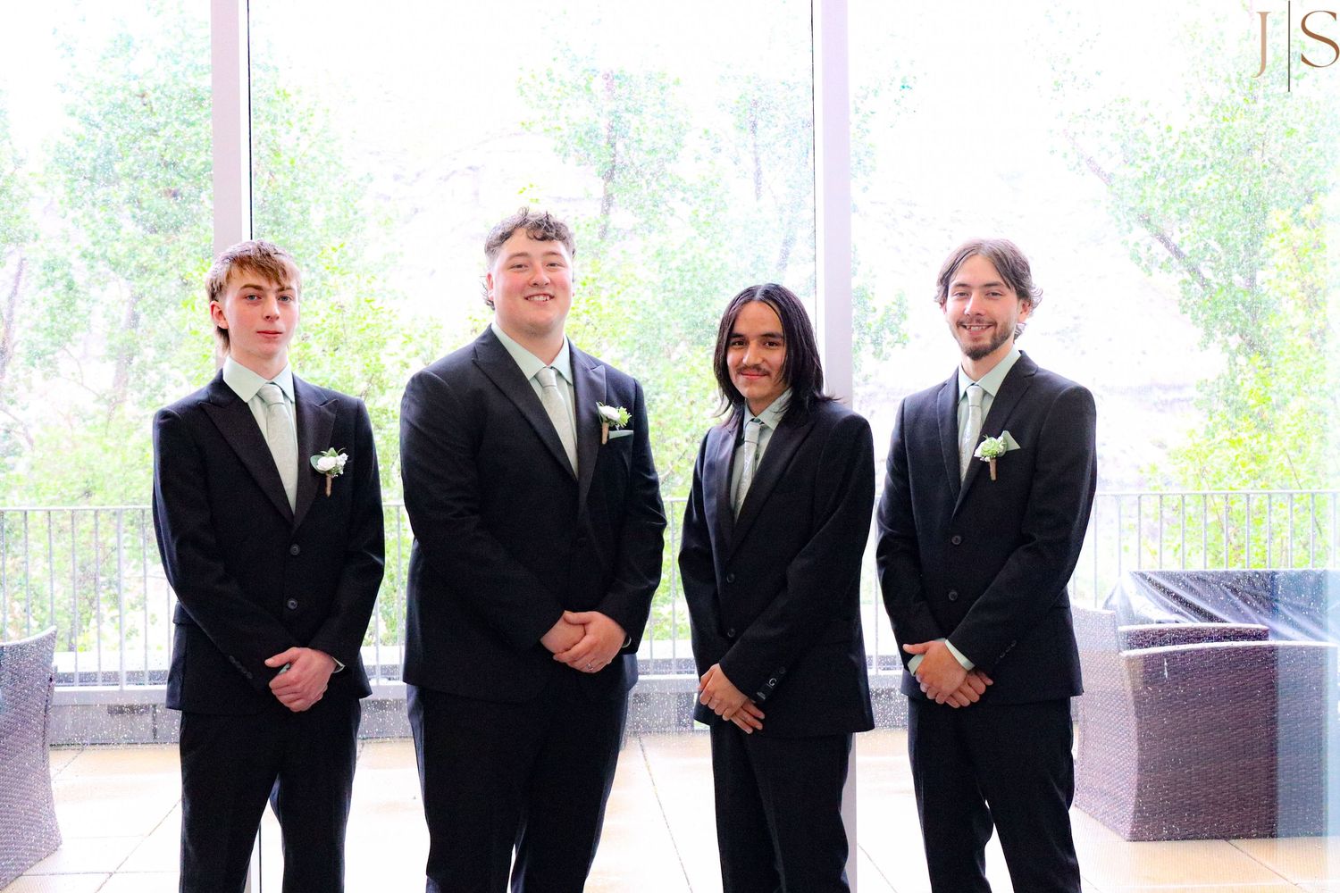 A group of four professionals in formal business attire stand together in front of bright windows.
