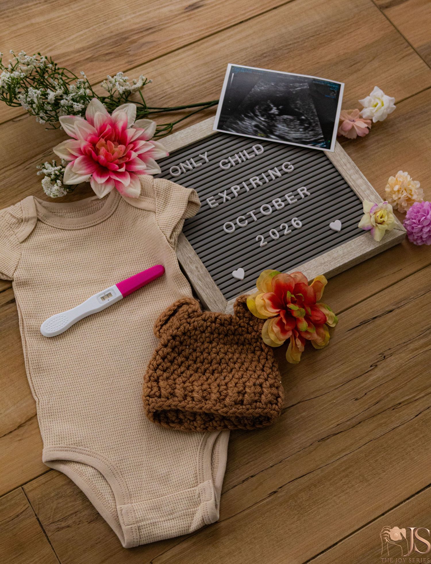 Pregnancy announcement flatlay with onesie, crochet bear hat, positive test, ultrasound, and letter board reading Only Child Expiring Octobe