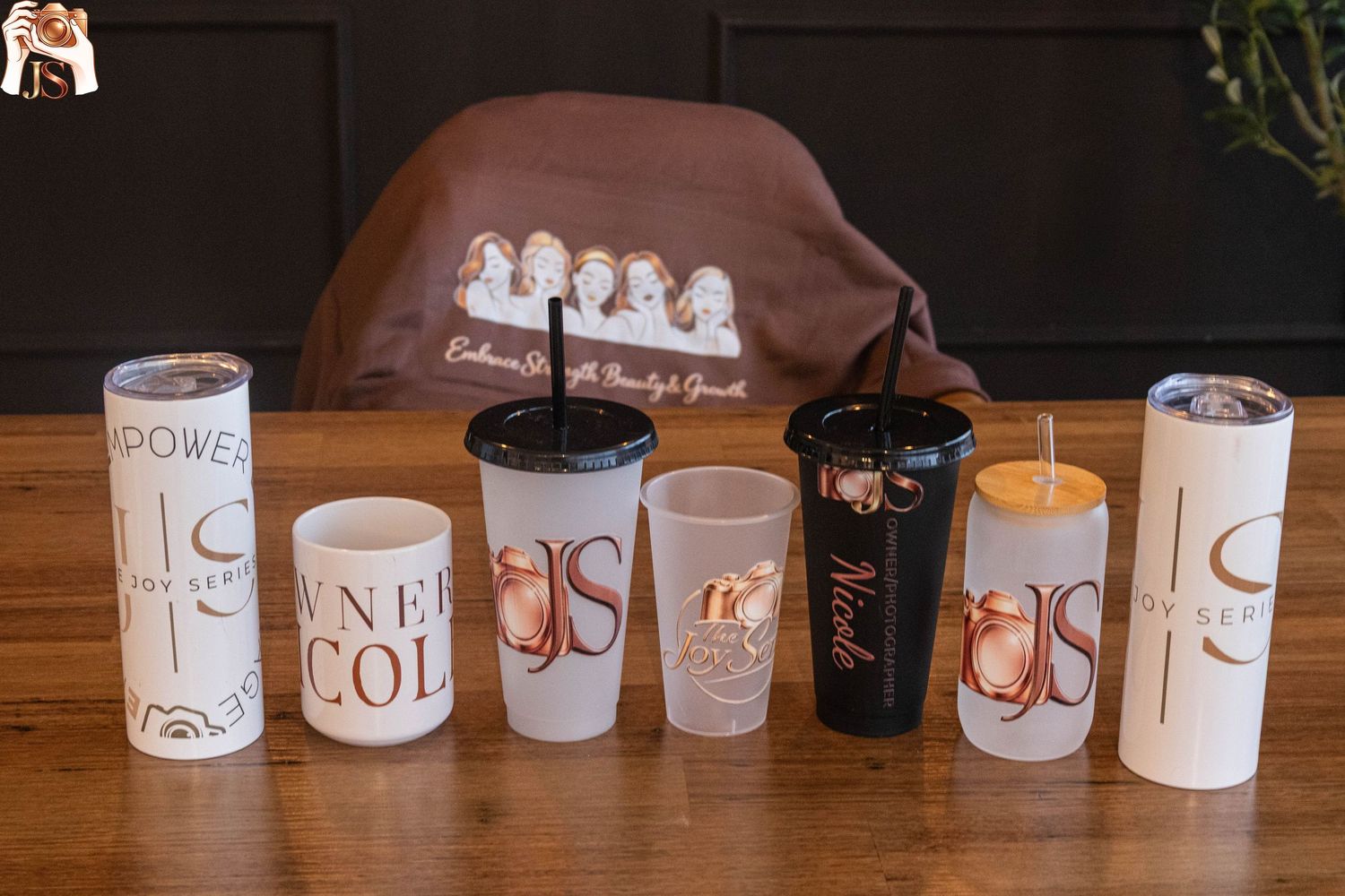 A series of white ceramic mugs with handwritten labels arranged in a row on a wooden table surface.