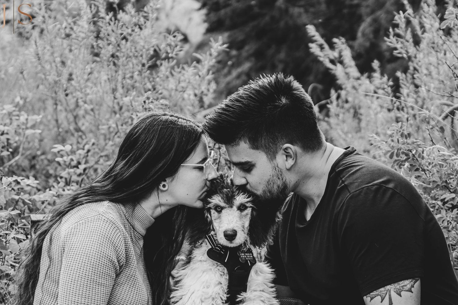 A couple shares a tender moment with their dog on a black and white portrait in nature.