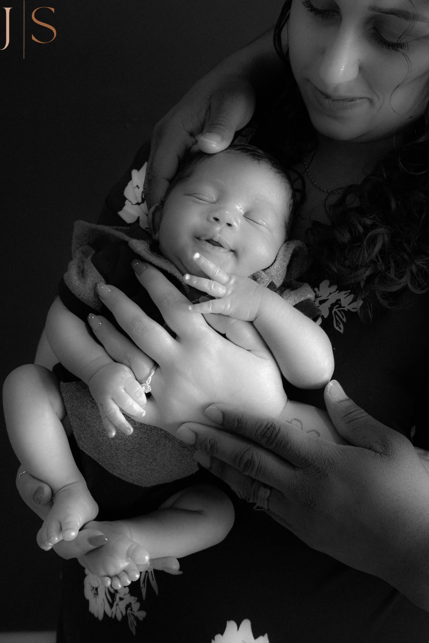 A peaceful black and white portrait of a sleeping newborn baby being gently cradled in caring arms.