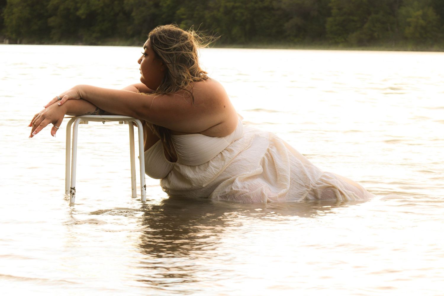 A person in a white wedding dress reclines in shallow water during a romantic bridal photo session at sunset.