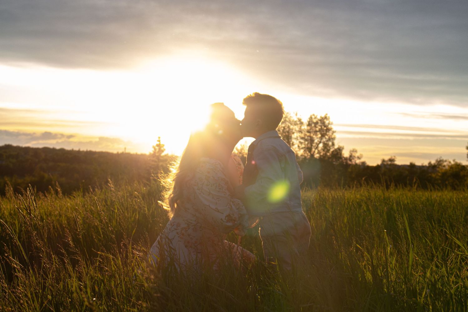 Sunset silhouette photo of couple embracing in tall grass.