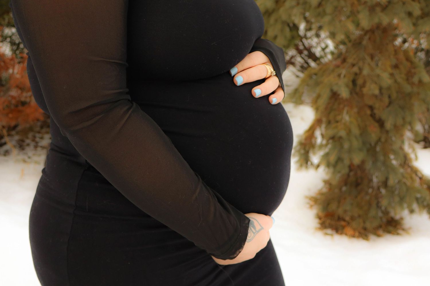 Side view of a pregnant belly in a black dress against an autumn backdrop.